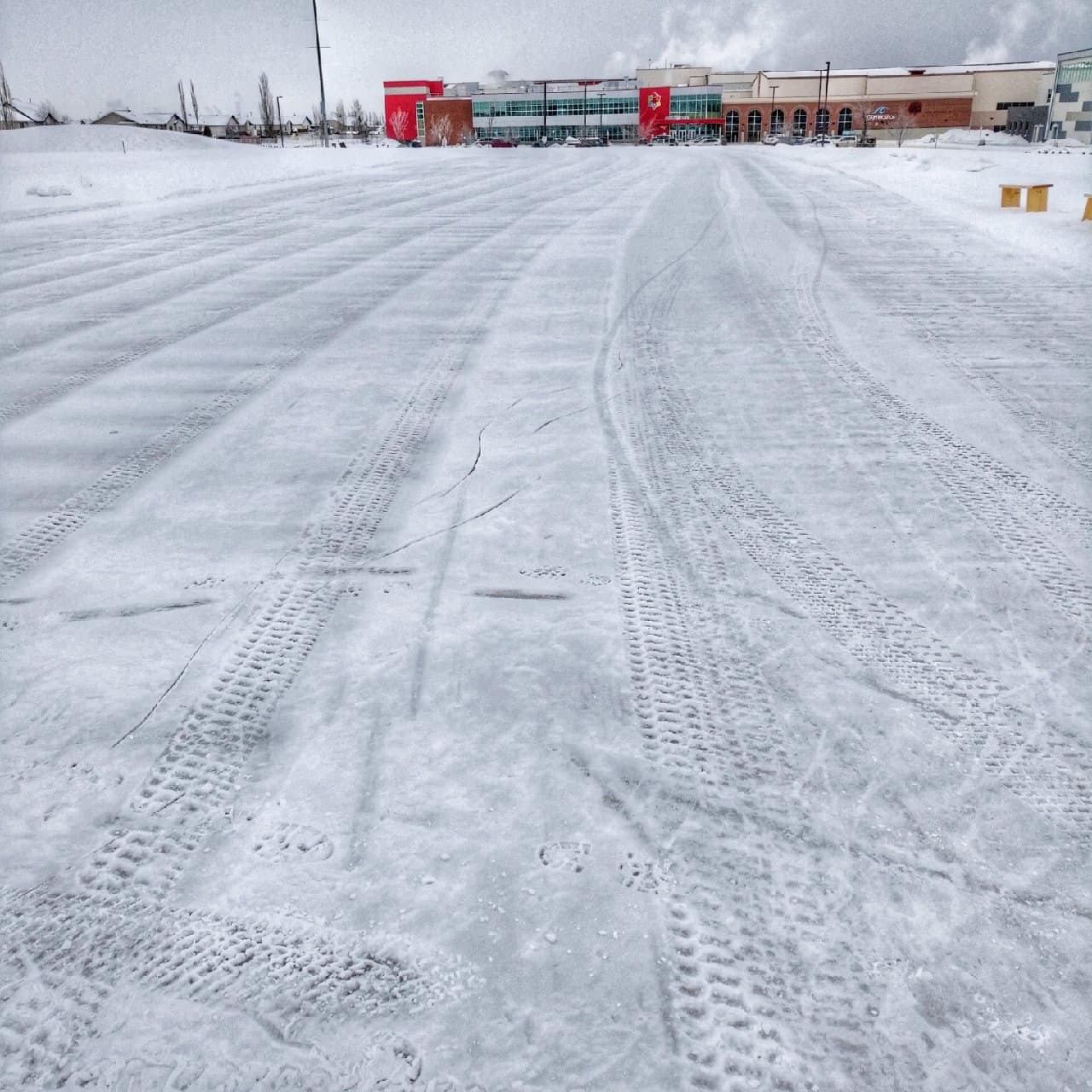Skating oval ice surface with tire tracks in front of community arena building.