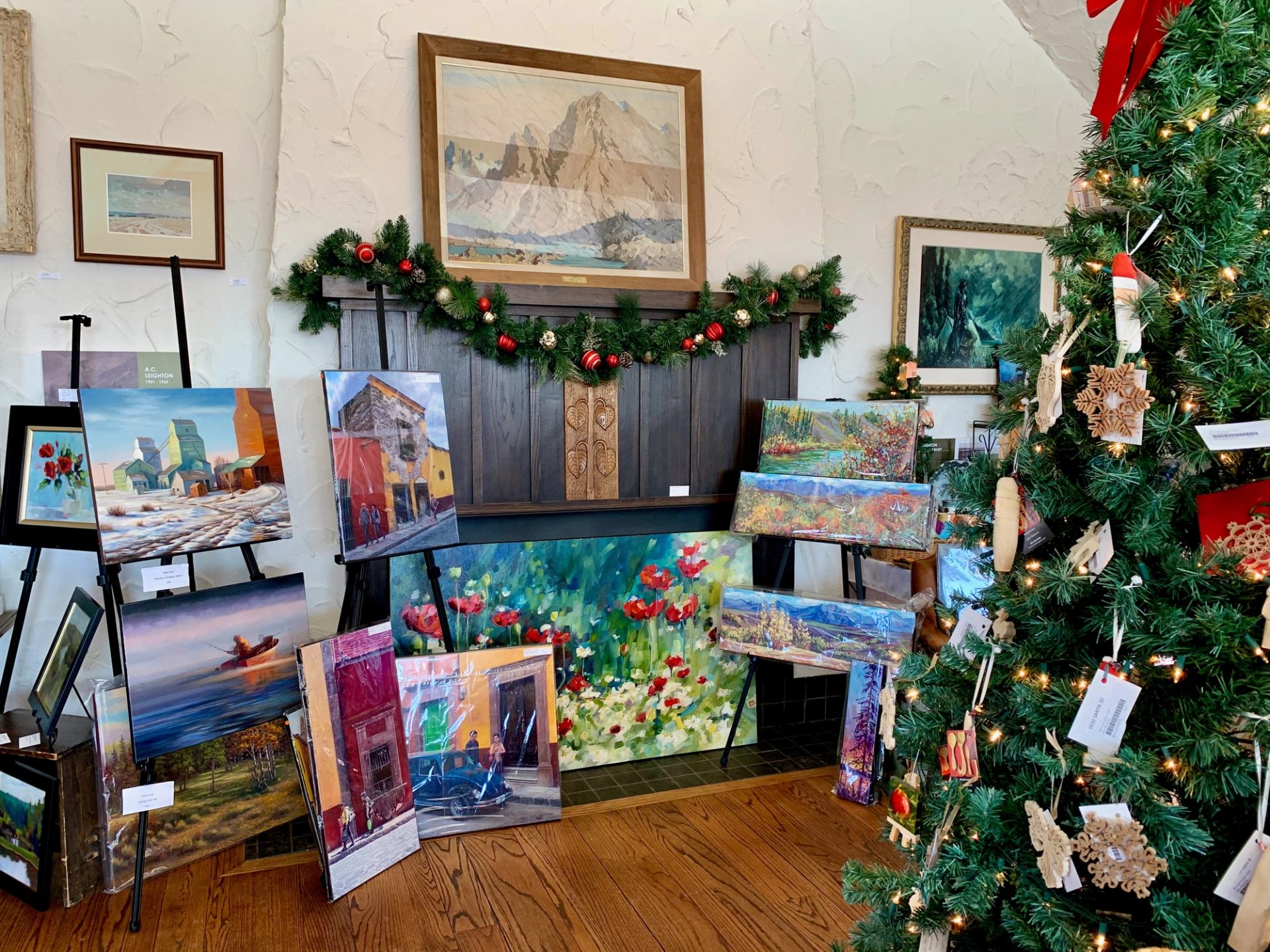 Holiday-decorated room with tree, fireplace, and artwork on display.