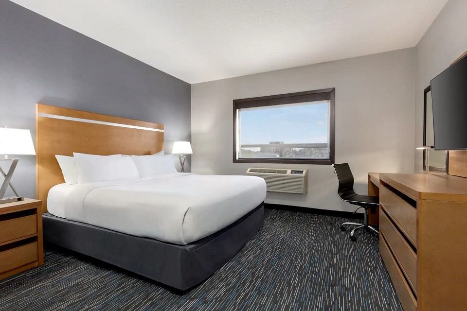Modern hotel room with king bed, desk, and large window at Wingate by Wyndham.