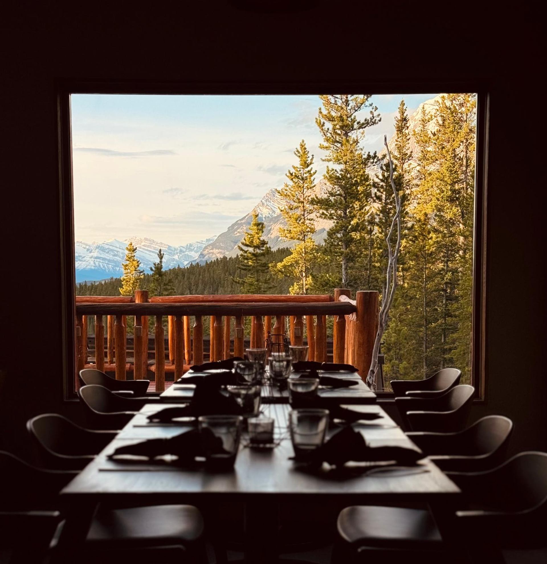 Dining table with mountain and pine forest view through a large window.