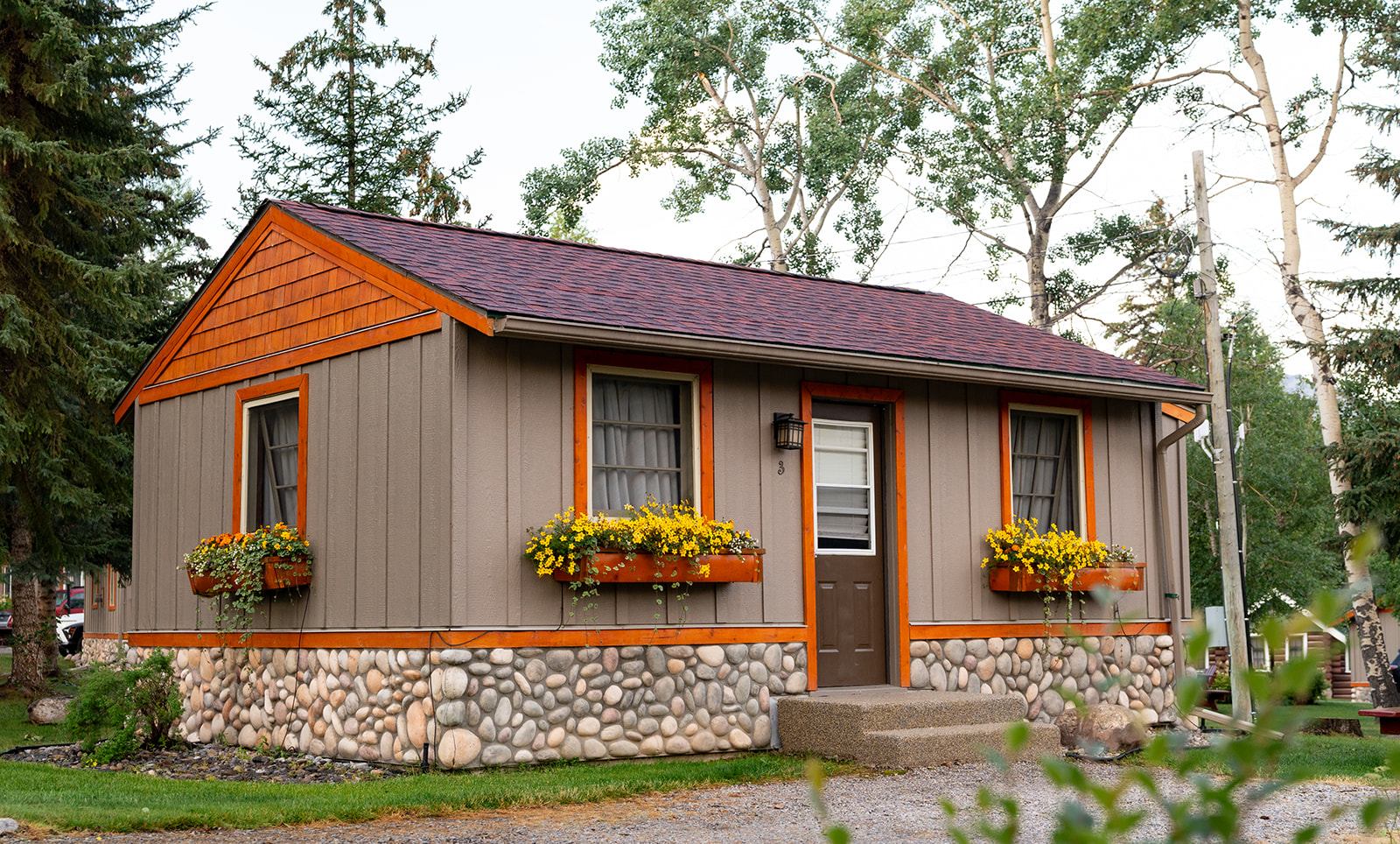 Rustic cabin with flower boxes, orange trim, and forest backdrop.