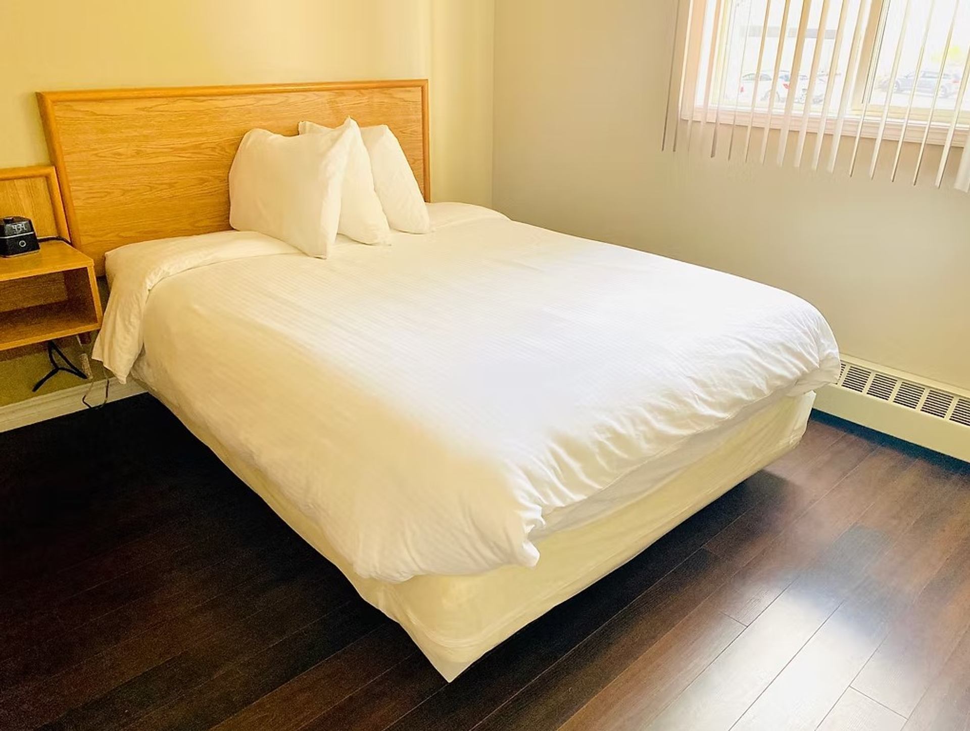 Guest room with a single bed, white linens, wood floors, and sunlight through a window.