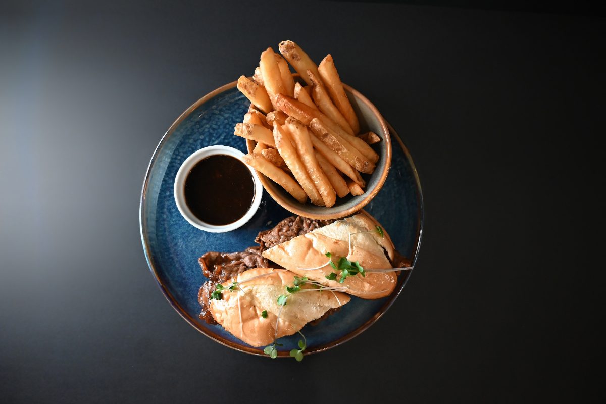 Sandwich with crispy fries and dark dipping sauce on a restaurant plate.