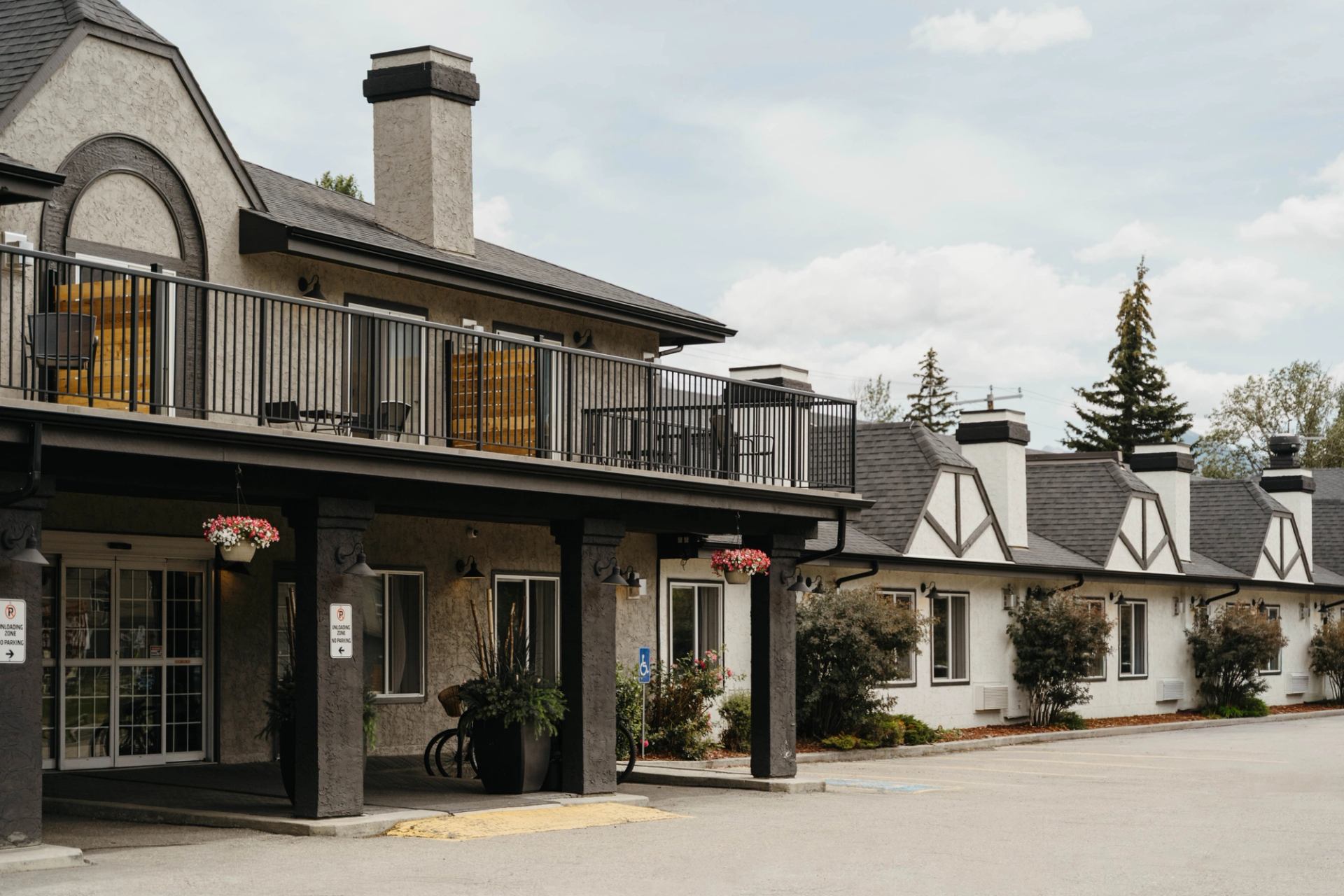 Two-storey motel exterior with balcony, hanging flower baskets and parking area in front.