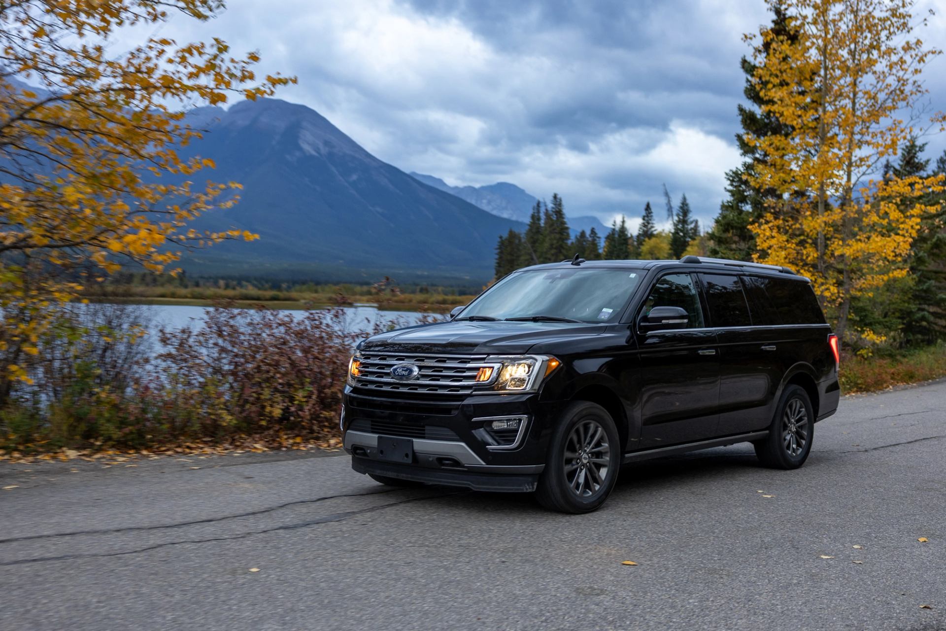 Black SUV on a paved road with colorful autumn trees and mountains under cloudy skies