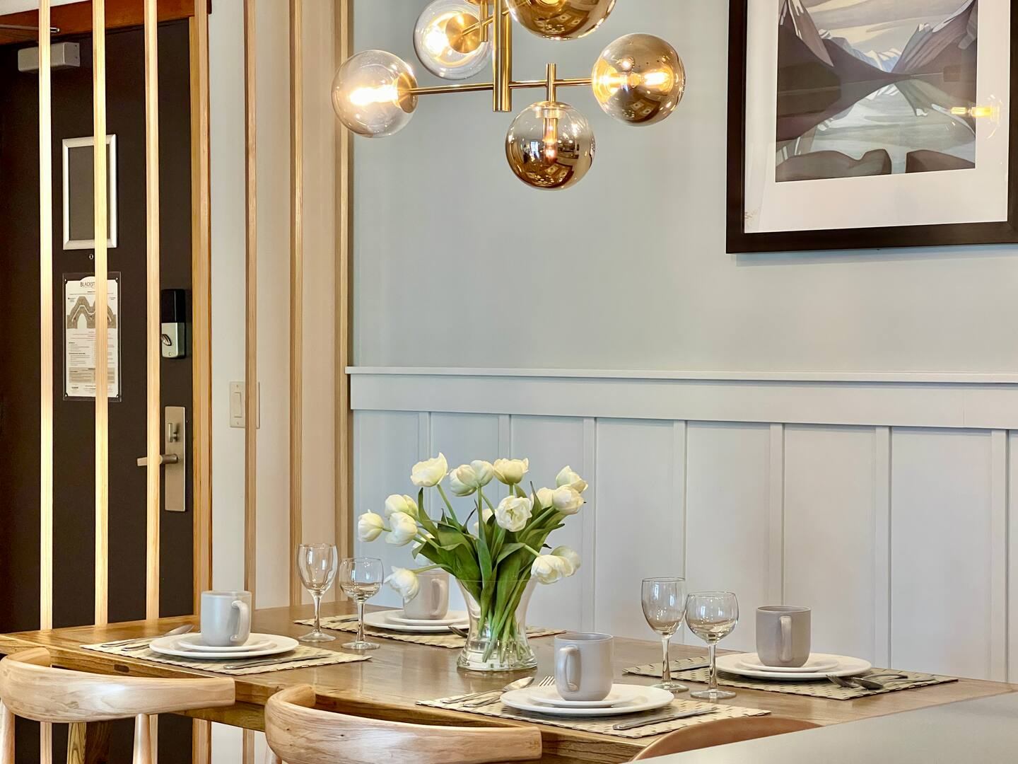 Dining table with tulip bouquet, place settings, wine glasses and modern gold light fixture.