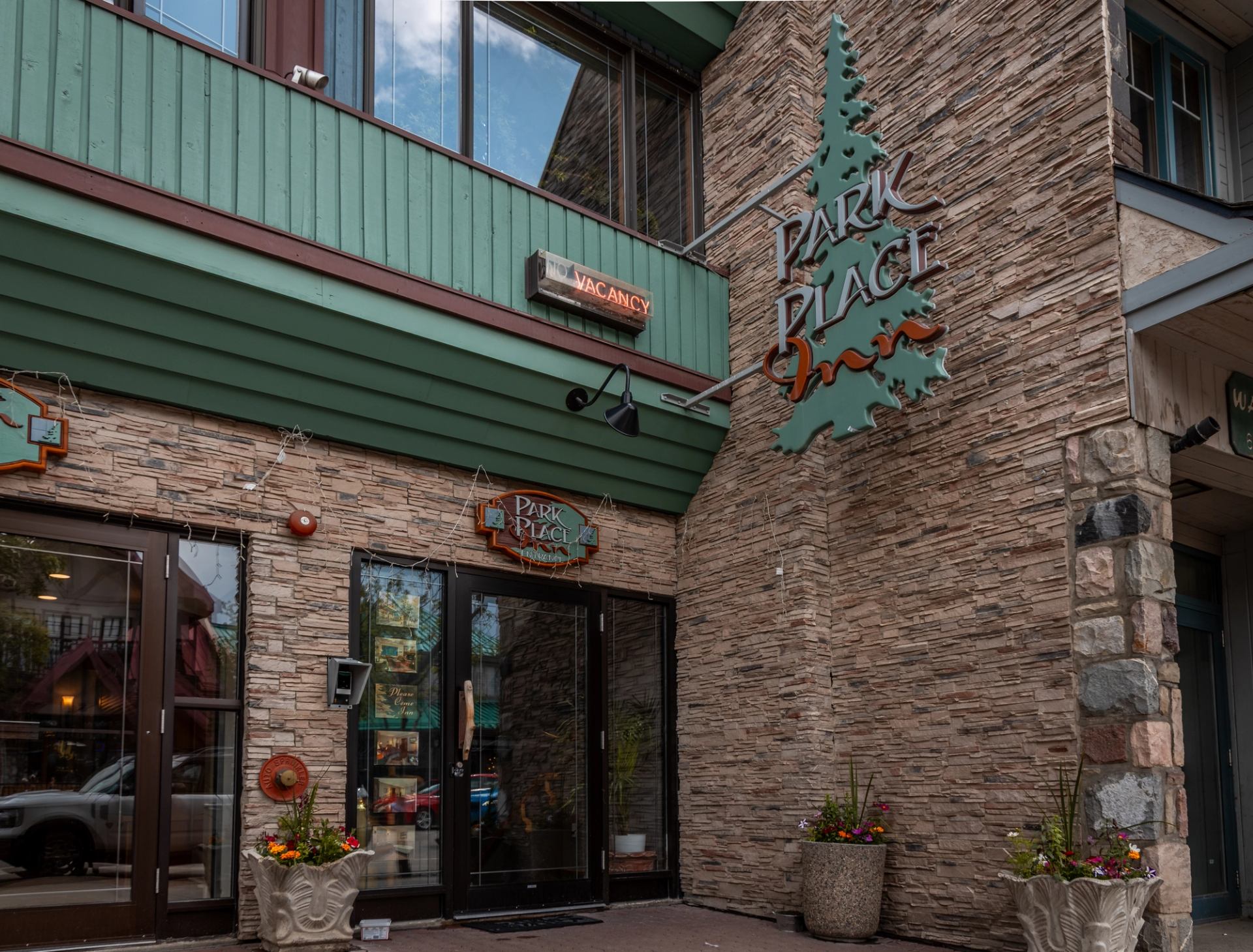 Entrance of Park Place Inn with green and stone exterior and potted plants.