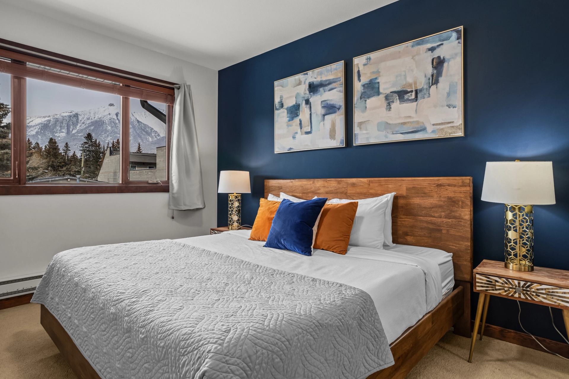 Bedroom with wooden bed, blue accent wall, mountain view window and abstract artwork.