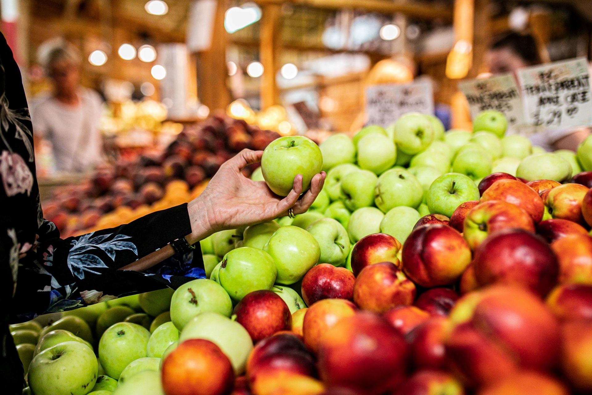 A shopper selects a green apple from a colorful fruit display at Calgary Farmers' Market South