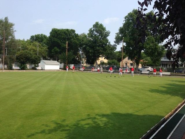 Red and white clad participants in the distance on a lawn bowling green.
