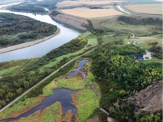 Aerial view of a lush river valley with a winding river on the left, fields in the distance, and a mix of forests and wetlands in the foreground. Peaceful and scenic.