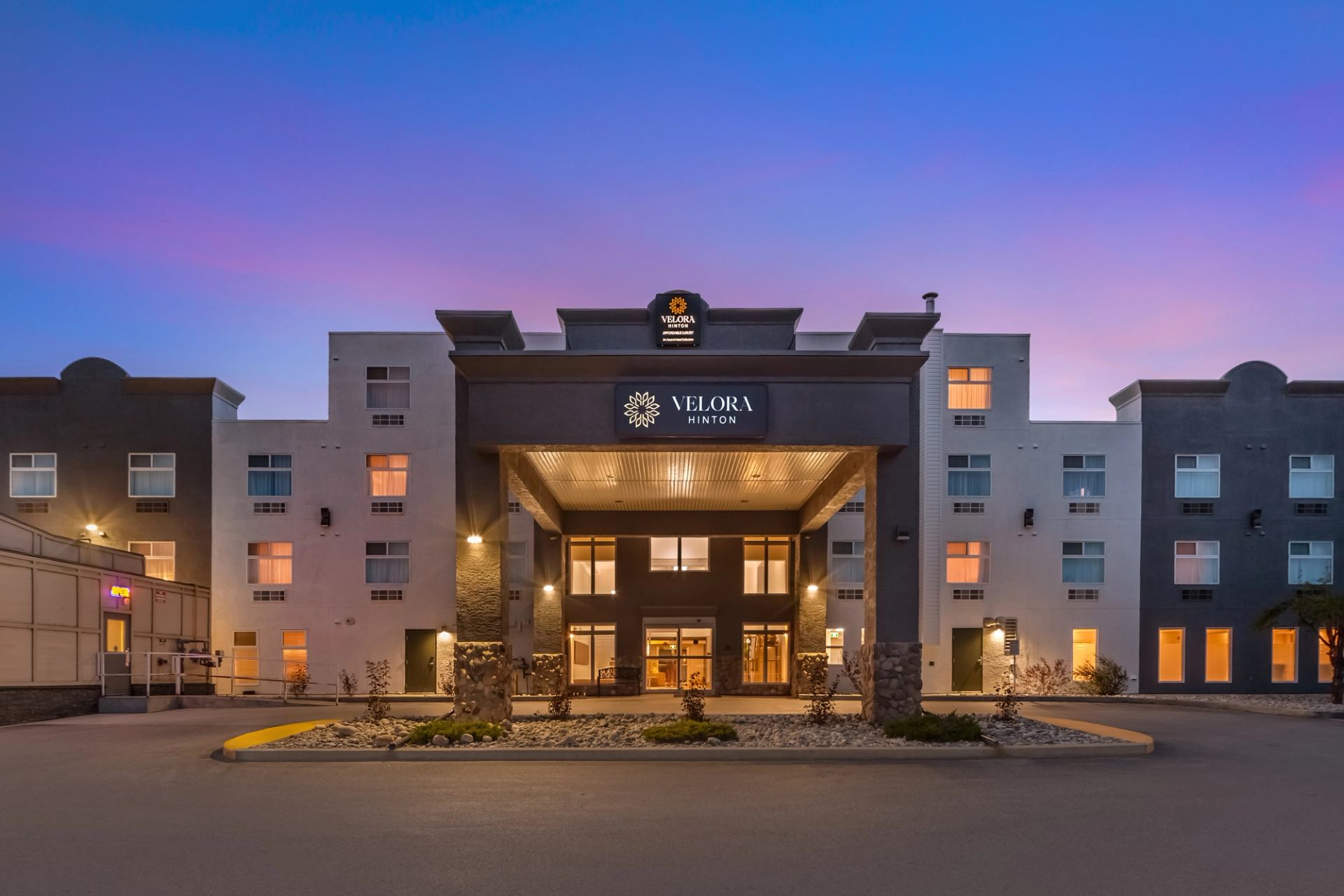 Exterior view of a modern hotel entrance at sunset with warm lighting.