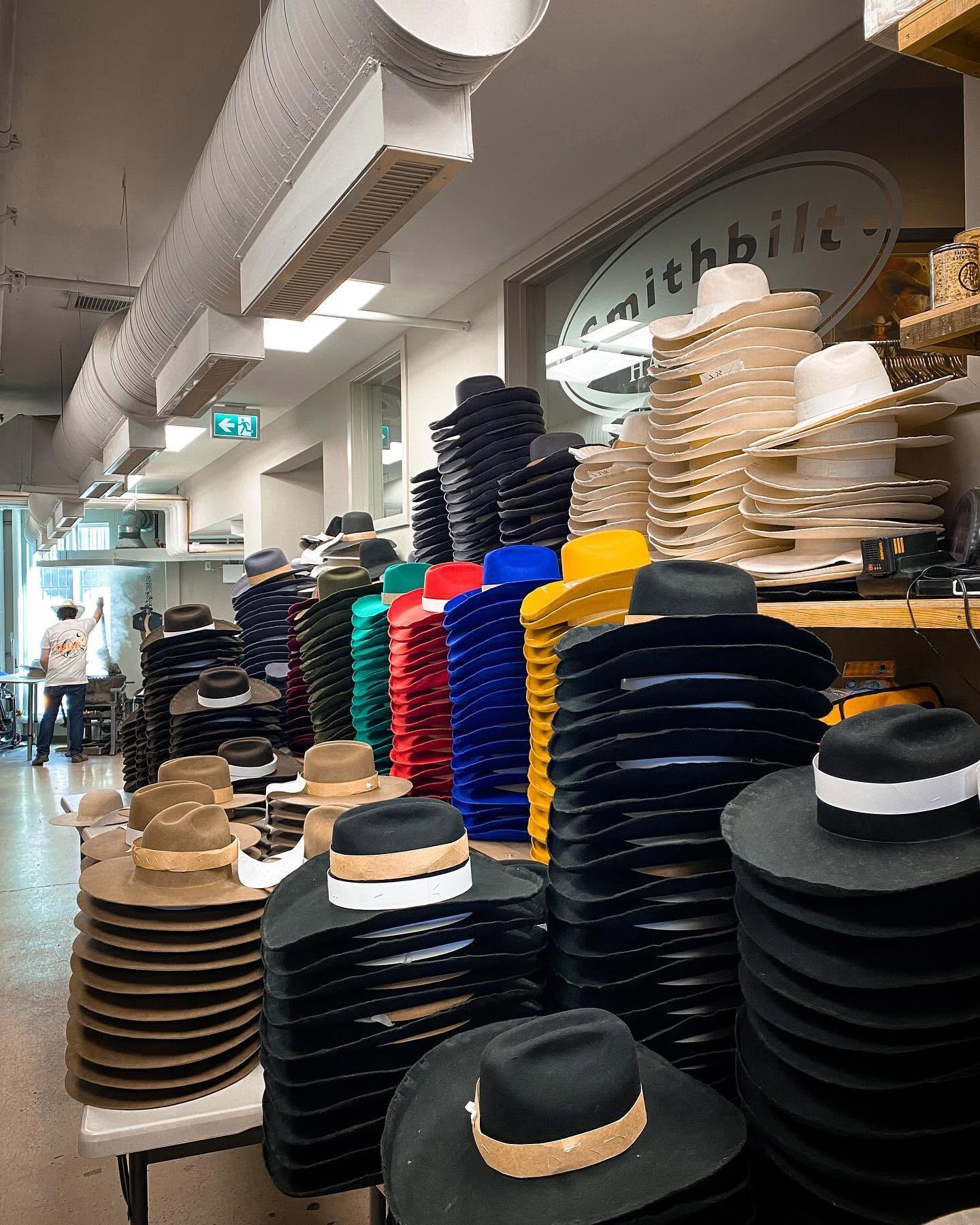 Stacks of colourful cowboy hats fill a workshop, with ventilation ducts overhead.