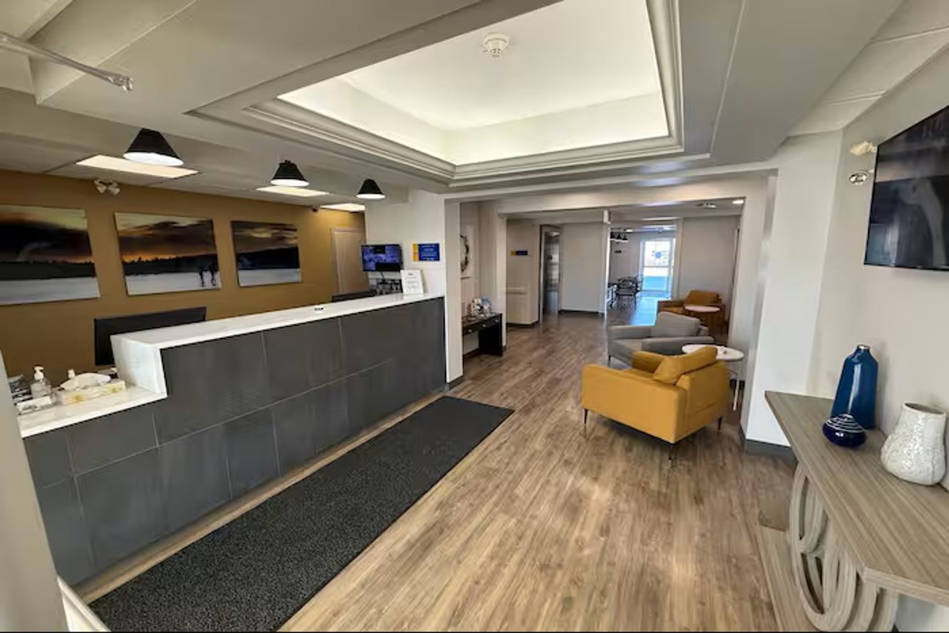Modern hotel lobby with reception desk, comfortable seating, wood flooring, and contemporary lighting.