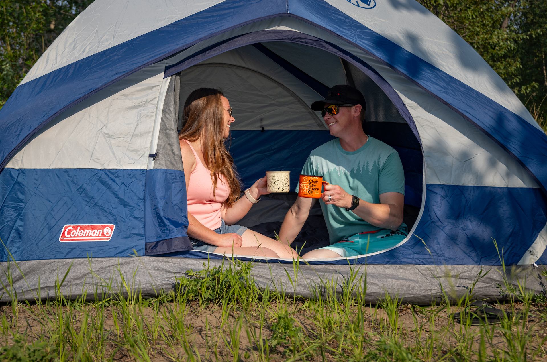 A man and women enjoying coffee in an open tent.