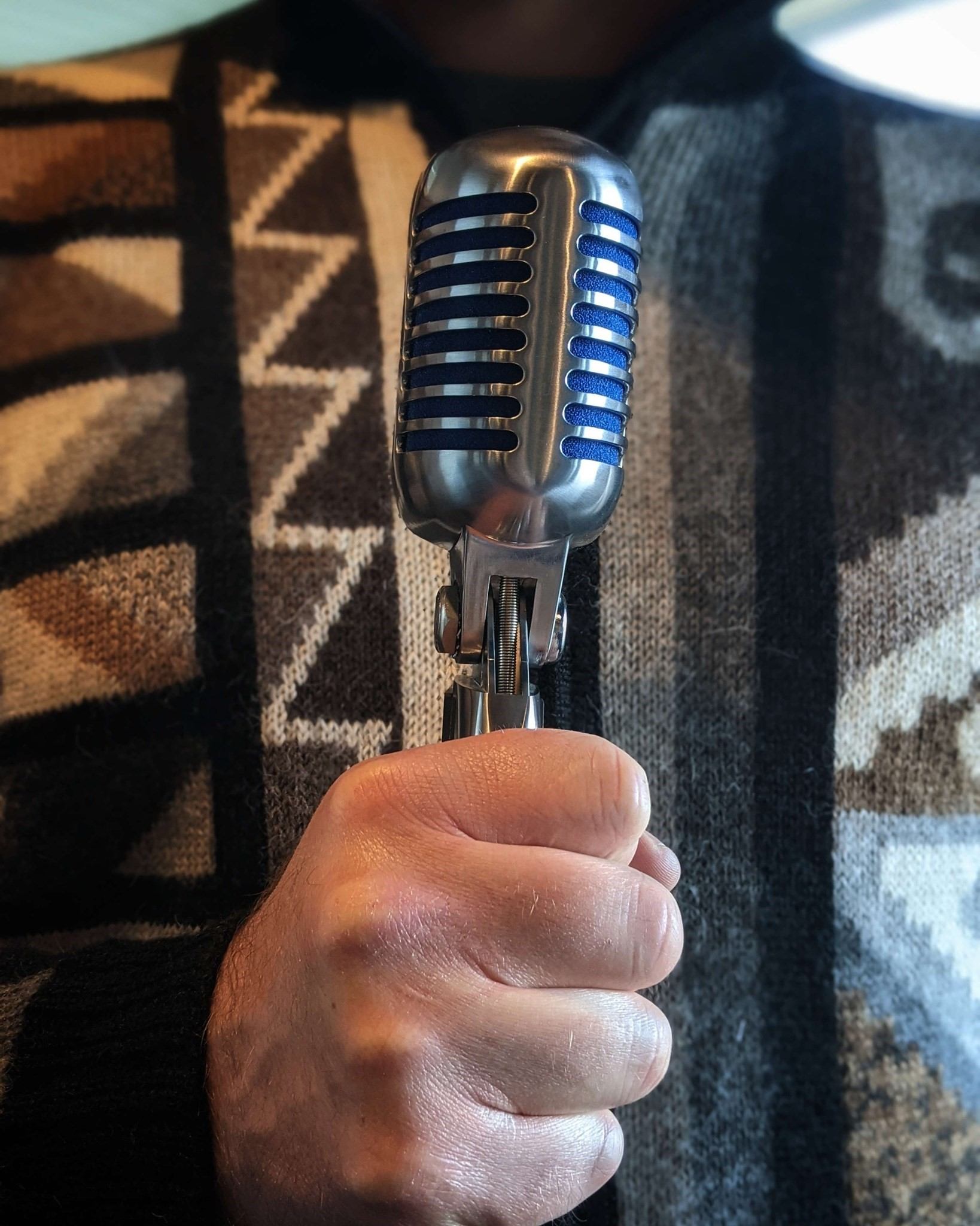 Person holding vintage mic in patterned sweater at Common Crown Brewing Co.