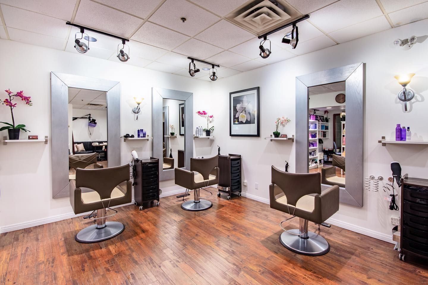 Hair salon interior with four styling chairs, mirrors, and wall-mounted track lights.