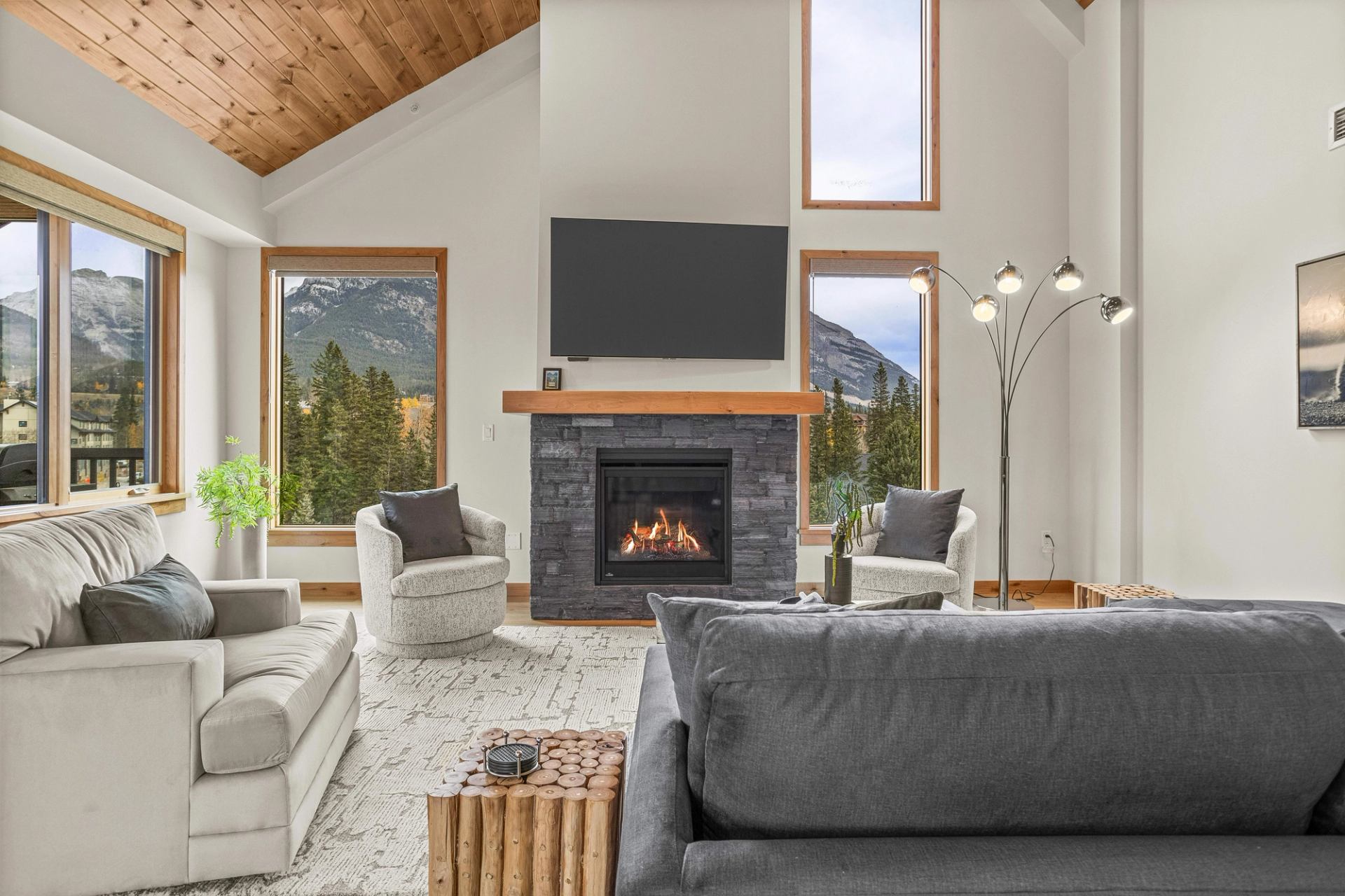 Living room with vaulted wood ceiling, stone fireplace and large mountain-view windows.