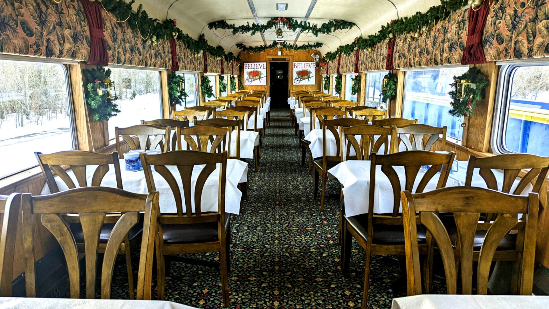 Dining railcar with wooden chairs, white tablecloths, wreaths and garlands.
