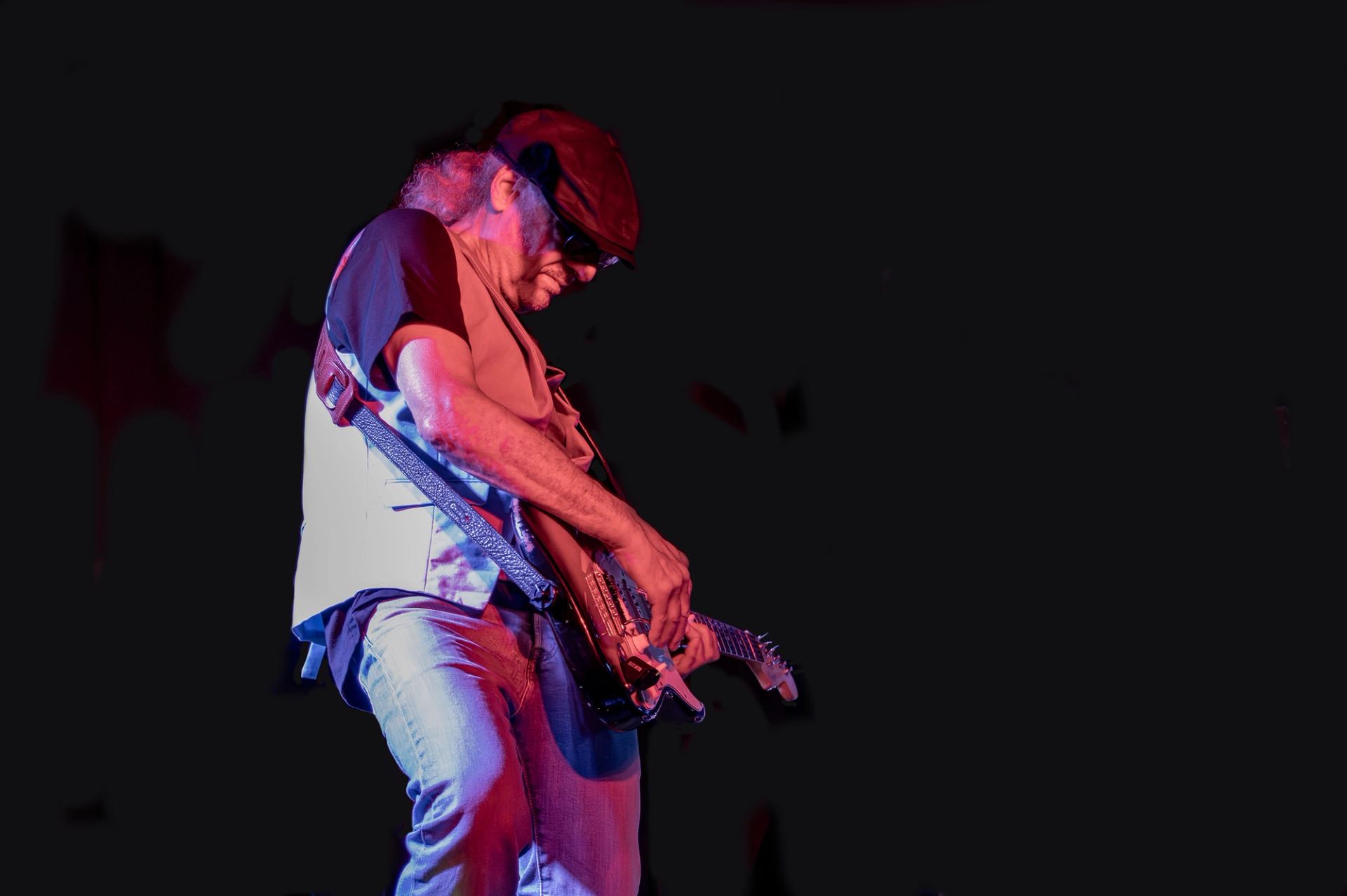 Guitarist in a cap performs under red and blue stage lighting.