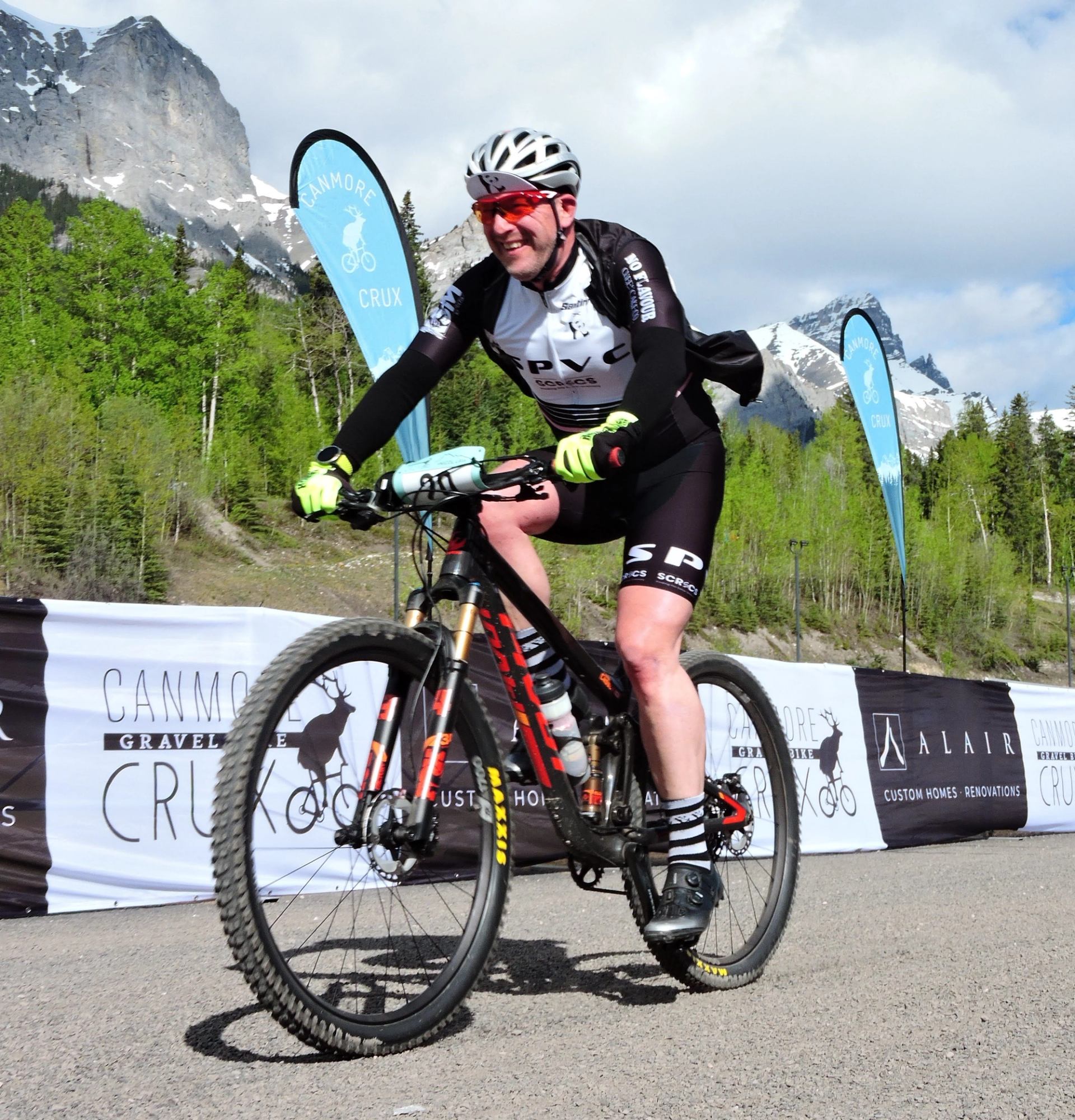A stunning aerial view of a cyclist navigating the scenic trails of the Canmore Crux, surrounded by the majestic Rocky Mountains.