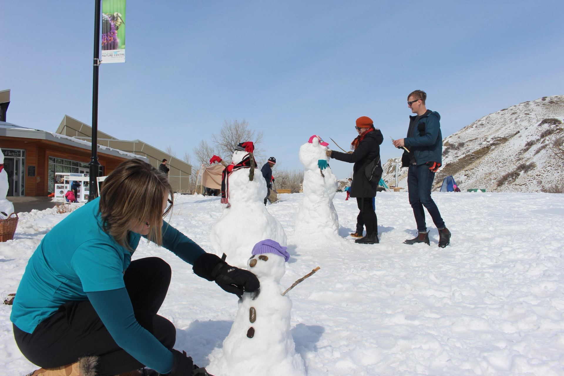 People building snowmen on a bright, snowy day.