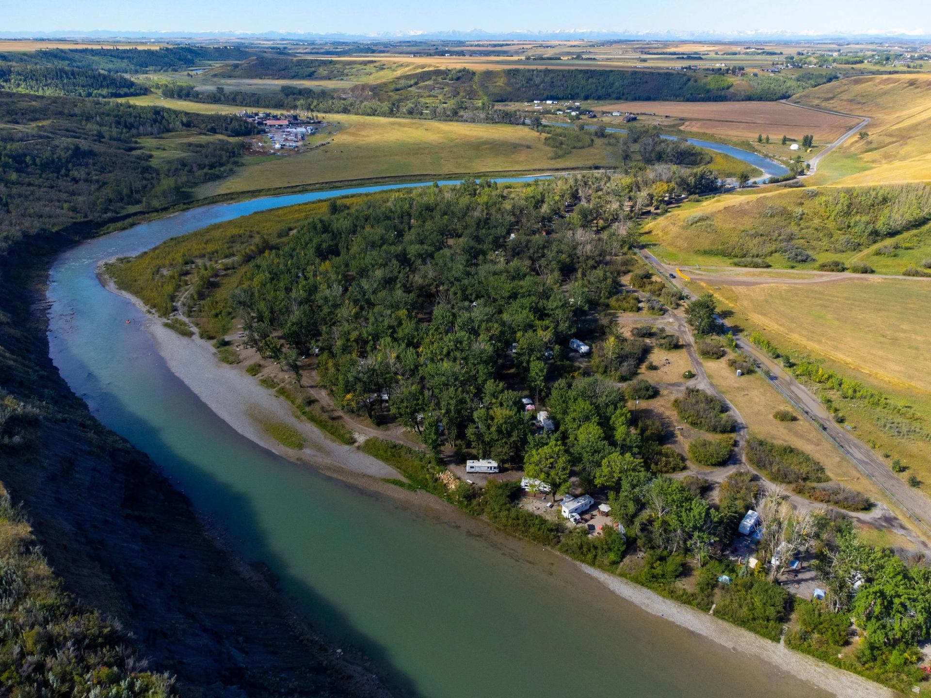 Aerial view of a river, camping area, and surrounding hills with green vegetation.