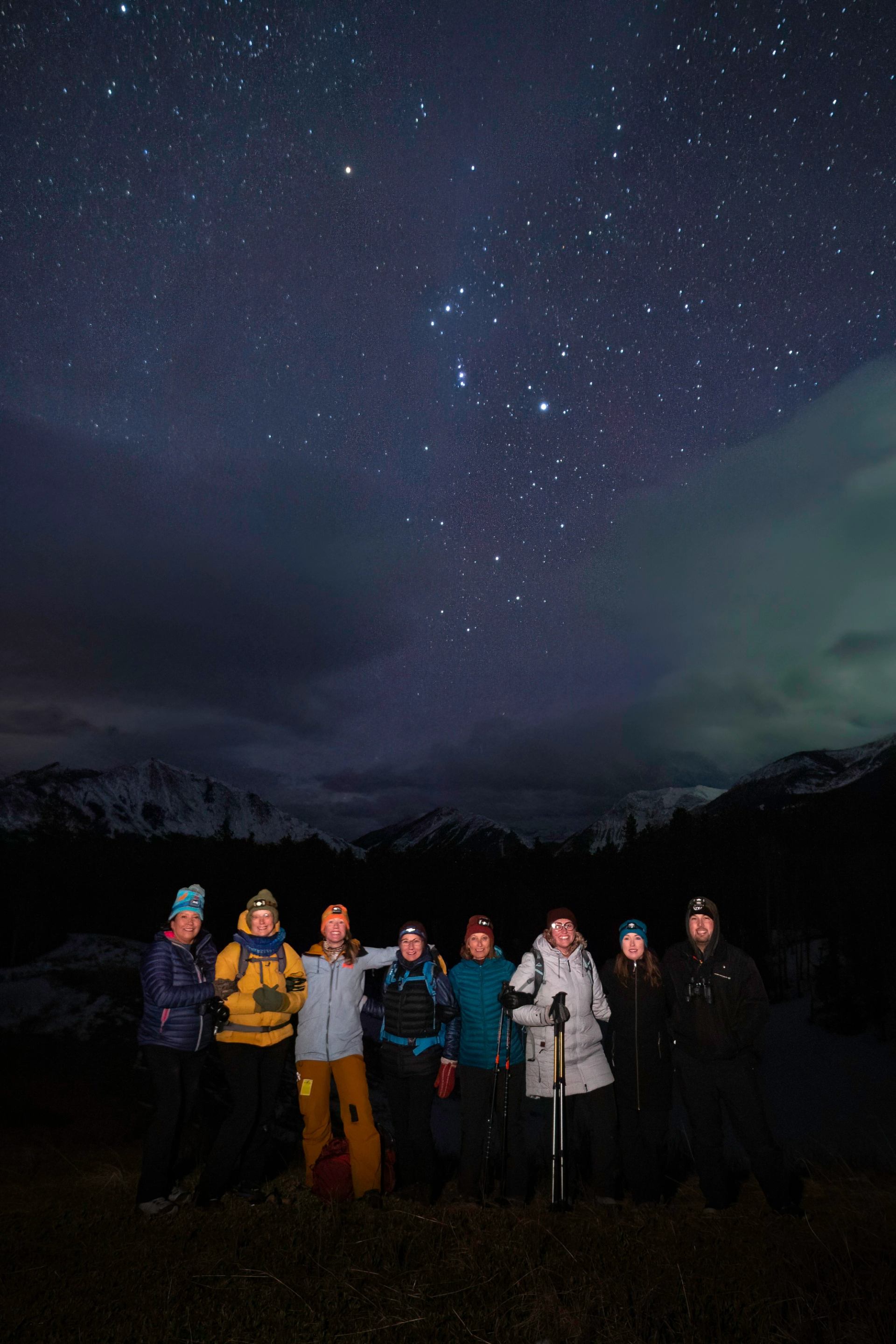 Group standing under a star-filled night sky with mountains faintly visible in the background.