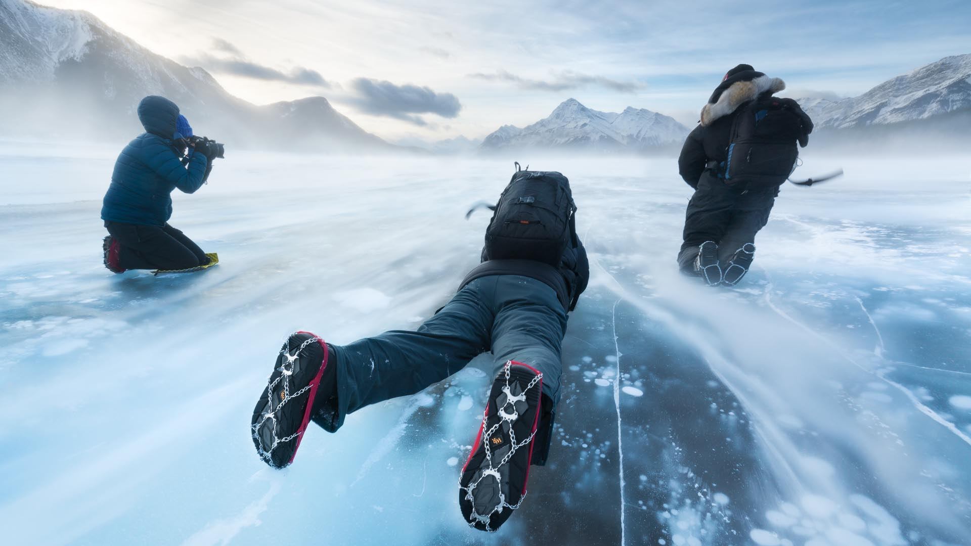 Photographers capture icy patterns while lying on frozen Abraham Lake surrounded by snowy peaks.