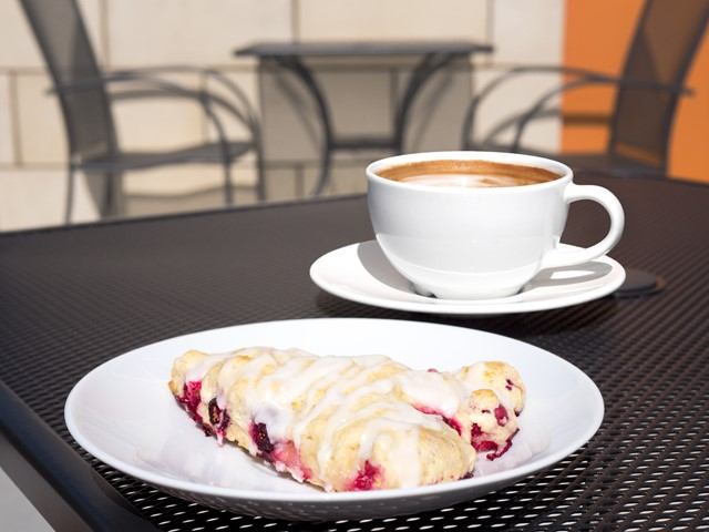 Pastry with icing on plate beside coffee cup on outdoor metal table.