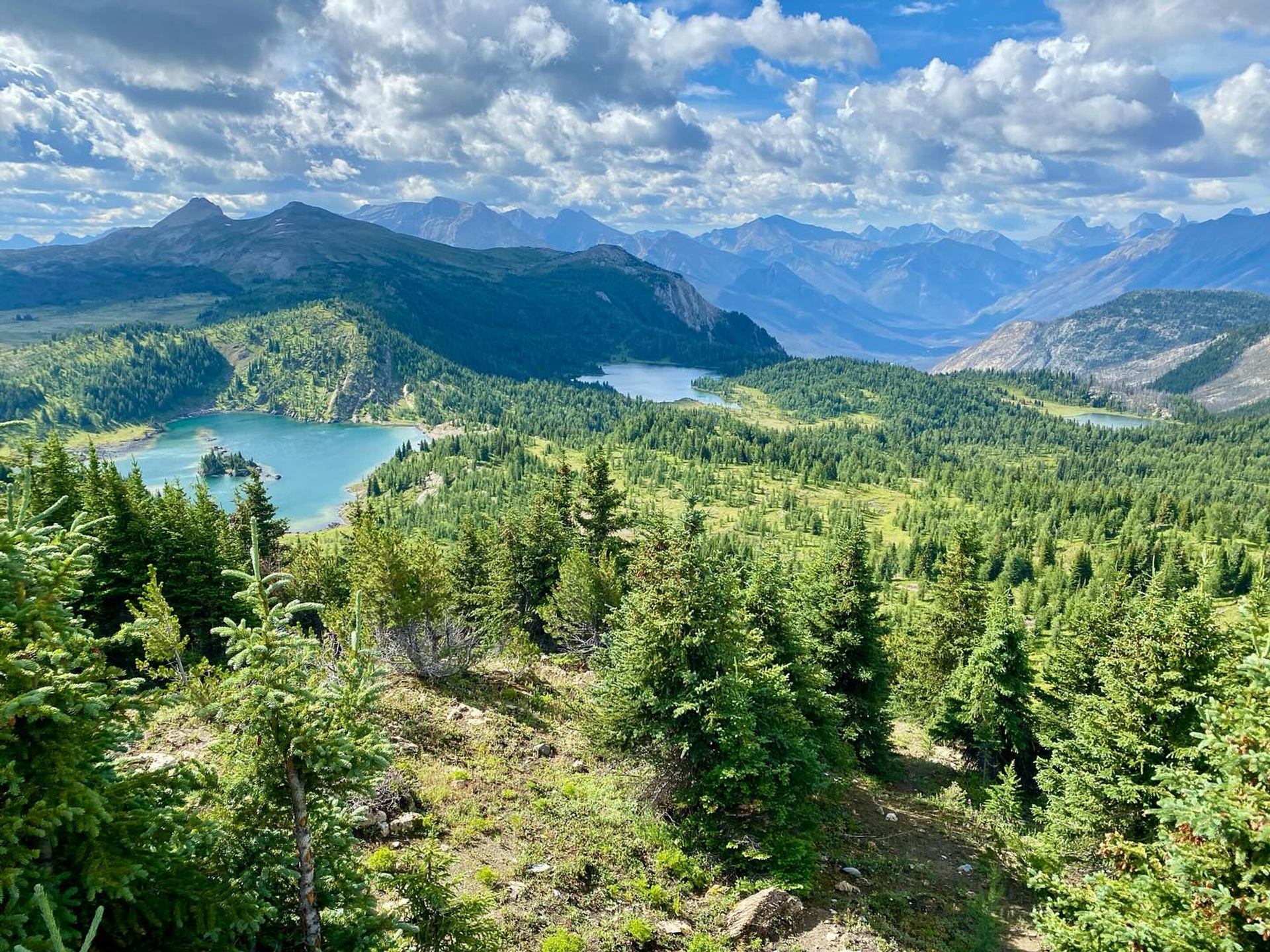 Turquoise alpine lakes amid evergreen forest and rugged mountains beneath billowing clouds.