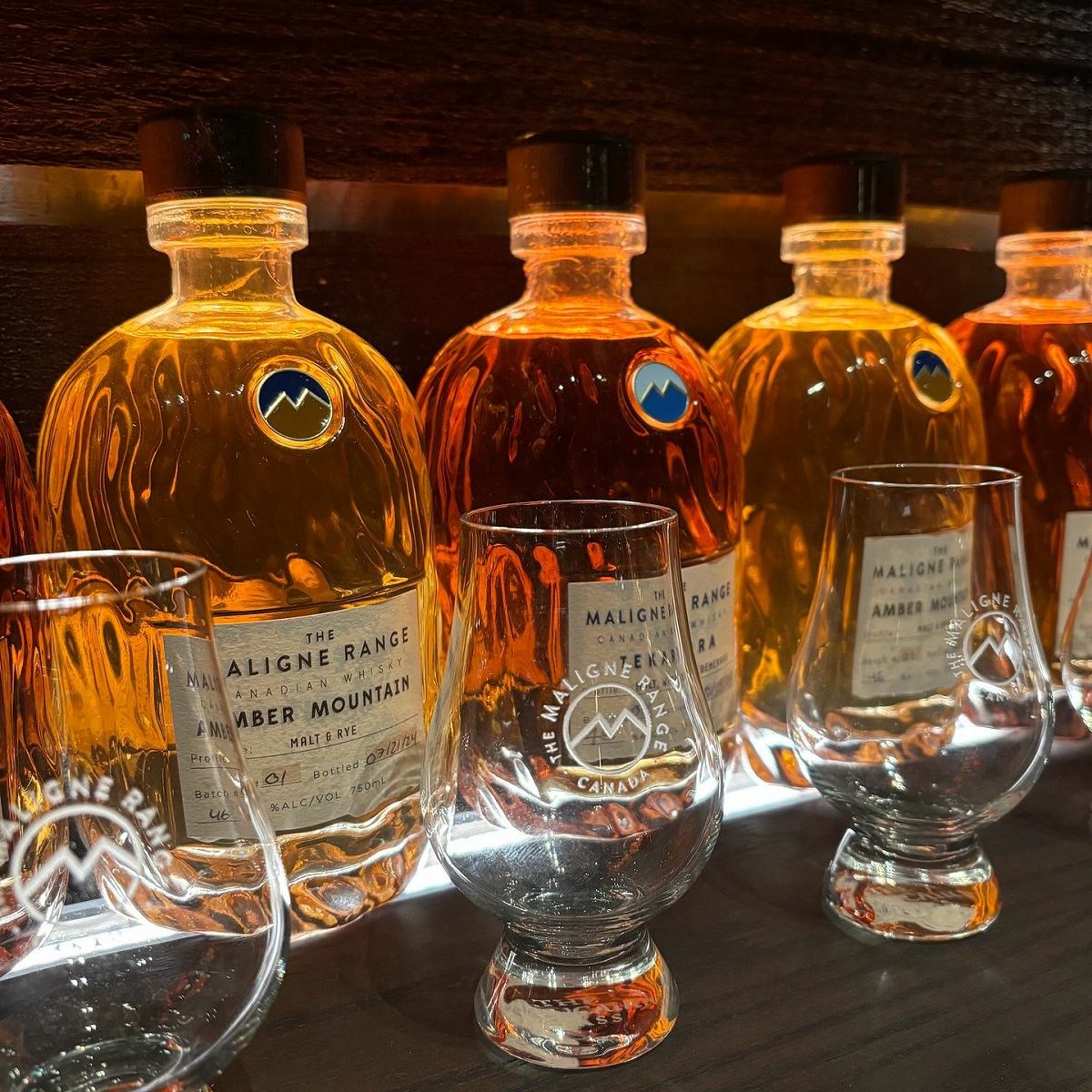 Bottles of whiskey lined up on a shelve with empty glasses in front.