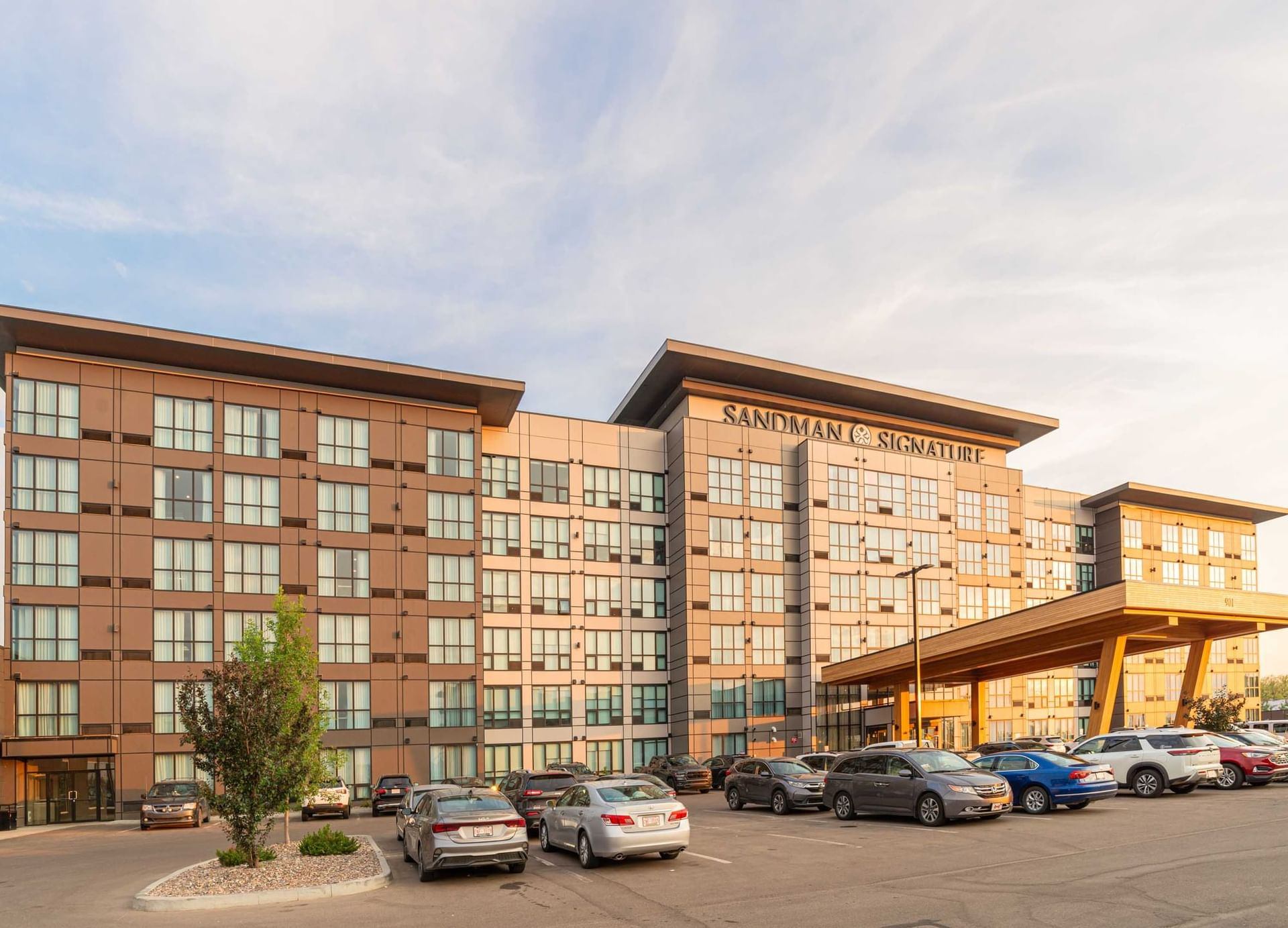 Front view of Sandman Signature Sherwood Park Hotel showing multi-story building, main entrance canopy, and parking lot with vehicles in front.