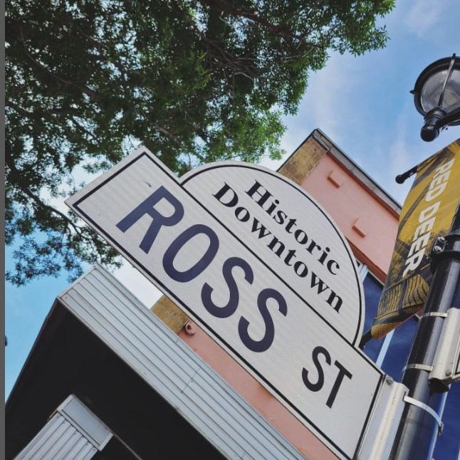 Street signs and banner in sunny downtown scene.