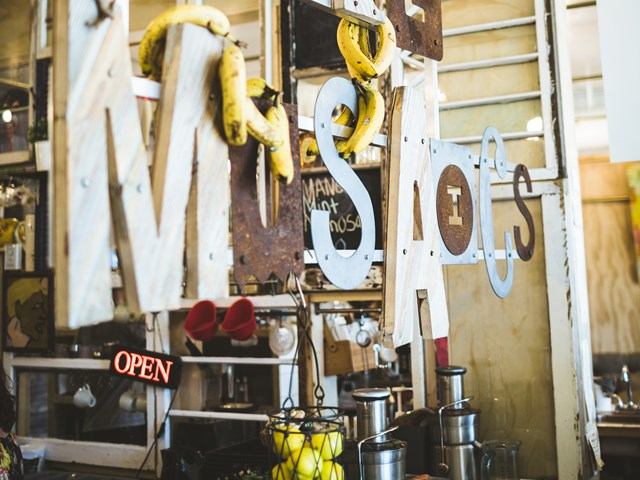 Café interior with rustic sign, hanging bananas, and basket of lemons.