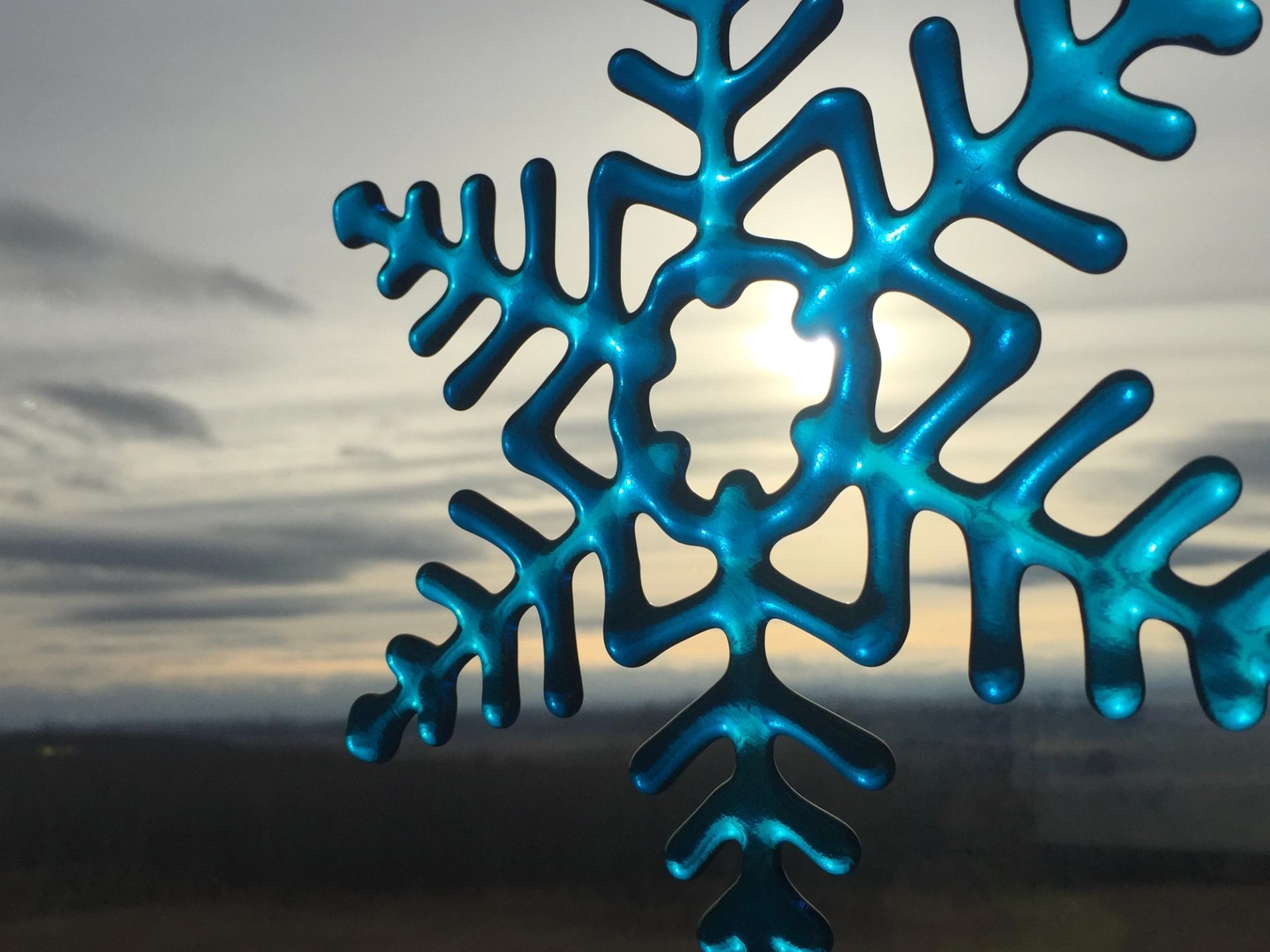 Blue snowflake ornament with sunlight shining through against a cloudy sky.