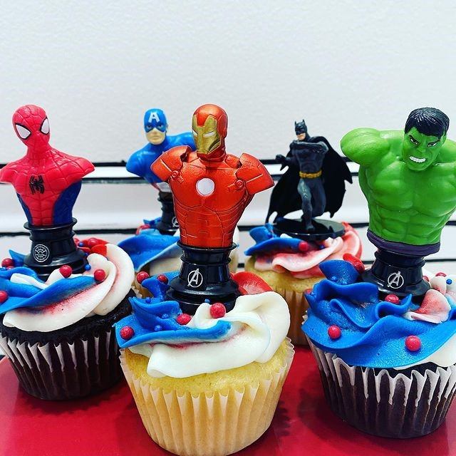 Cupcakes topped with colorful superhero figurines and red, white, and blue swirled frosting.