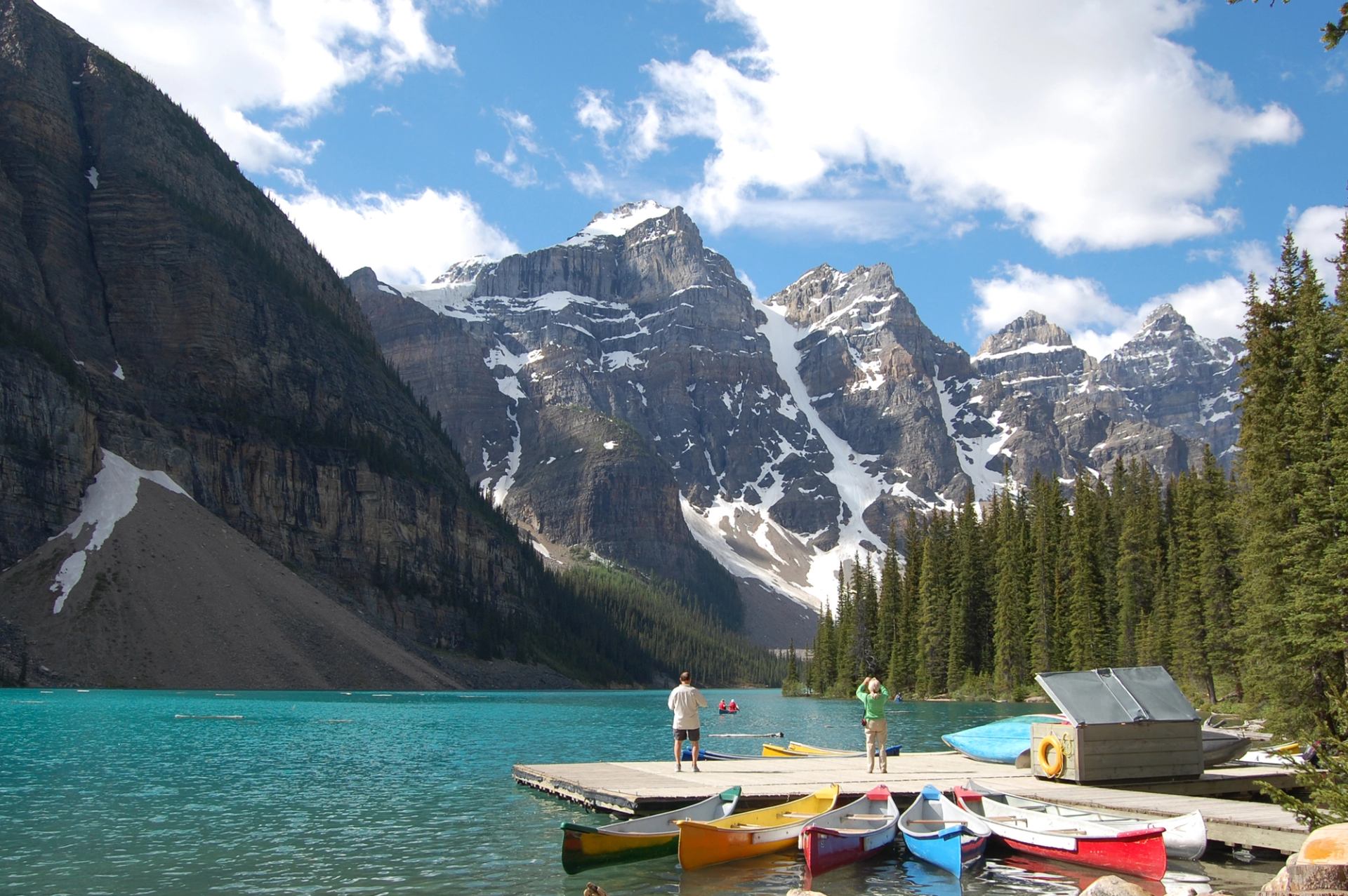 A dock with colorful canoes on a bright turquoise lake surrounded by high peaks.