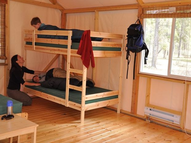 Mother tucking kids into a bunk bed in a cabin at Whistlers Campground.