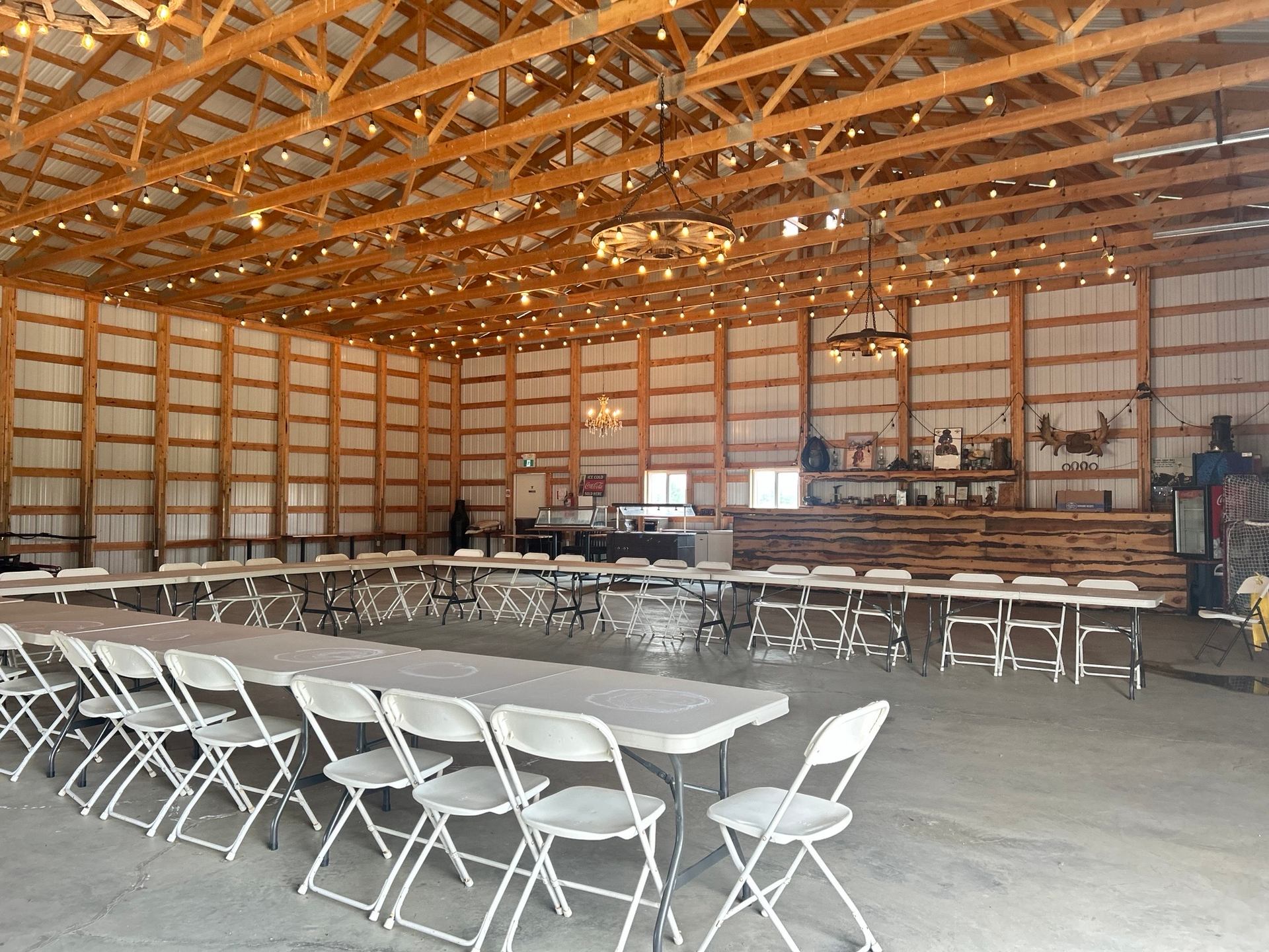 Indoor mini-golf venue with rows of tables and chairs under wooden beams and string lights.