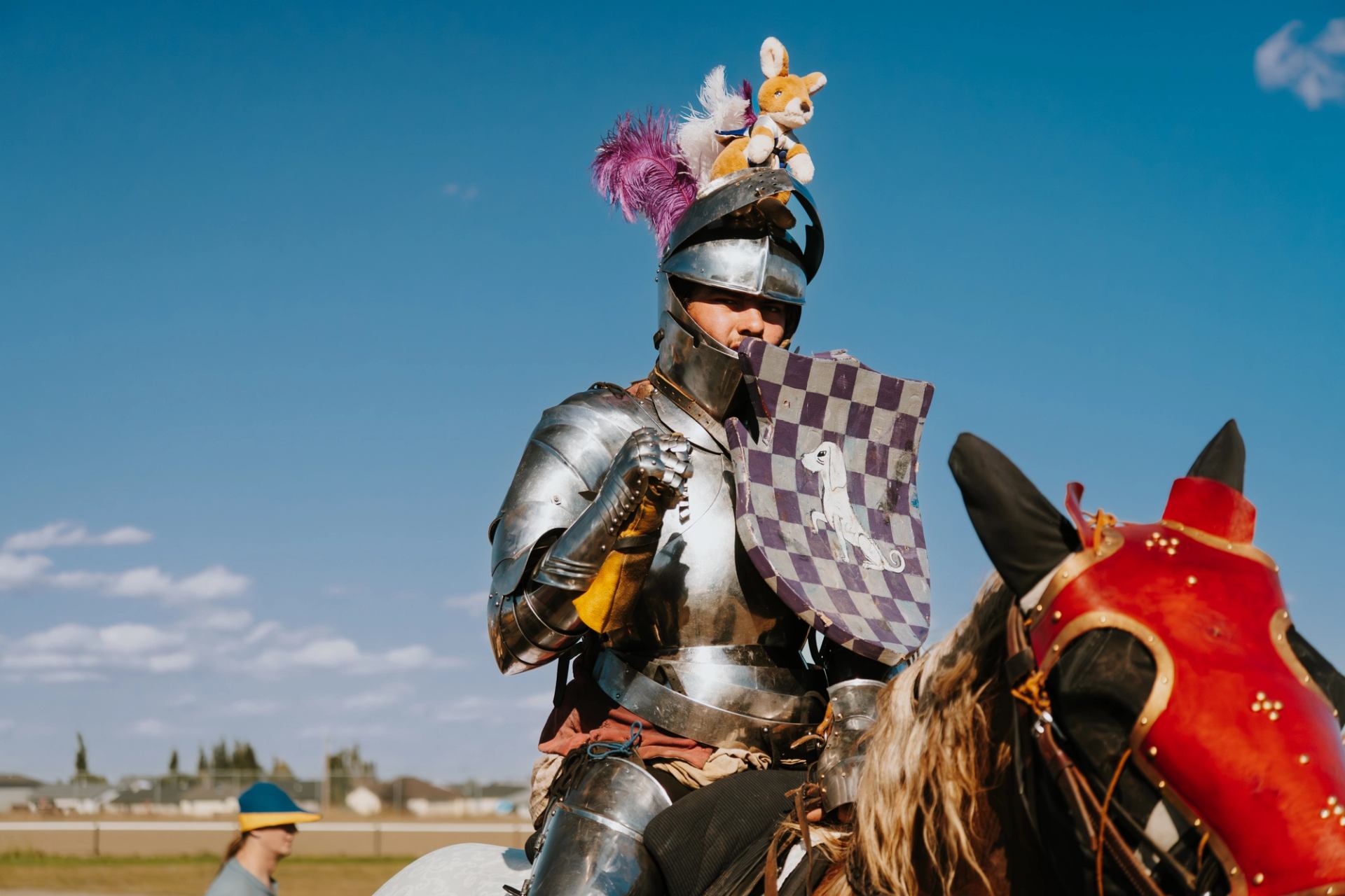 Knight in armor with plush toys on helmet rides horse at Vegreville Medieval Faire.