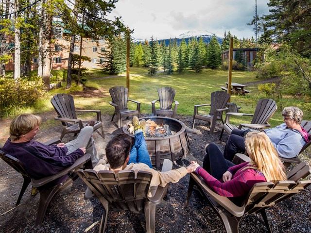 Group sits around a fire pit with mountains and trees in the background.