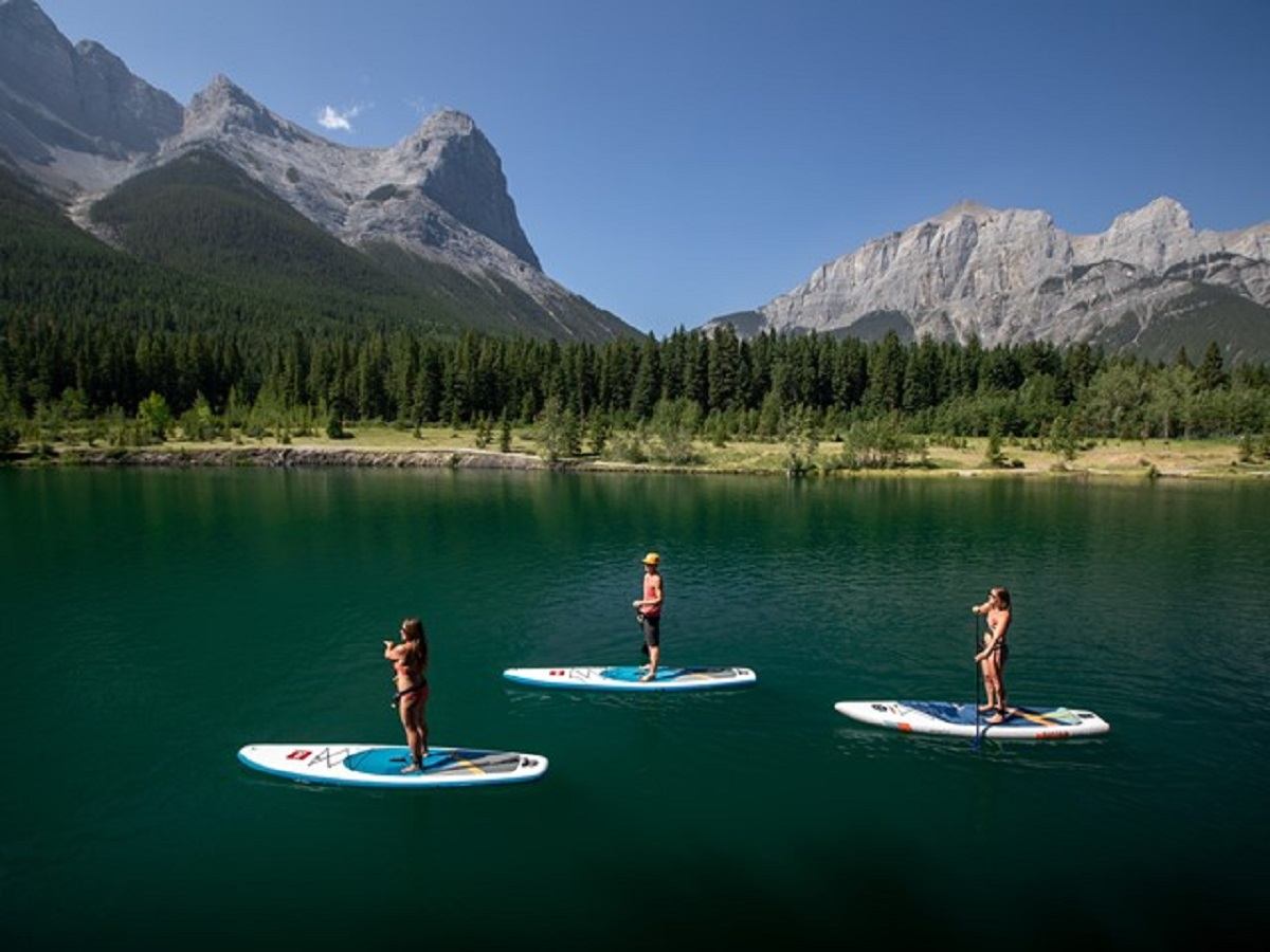 Paddleboarders on a clear lake with forest and mountain views in Bow Valley.