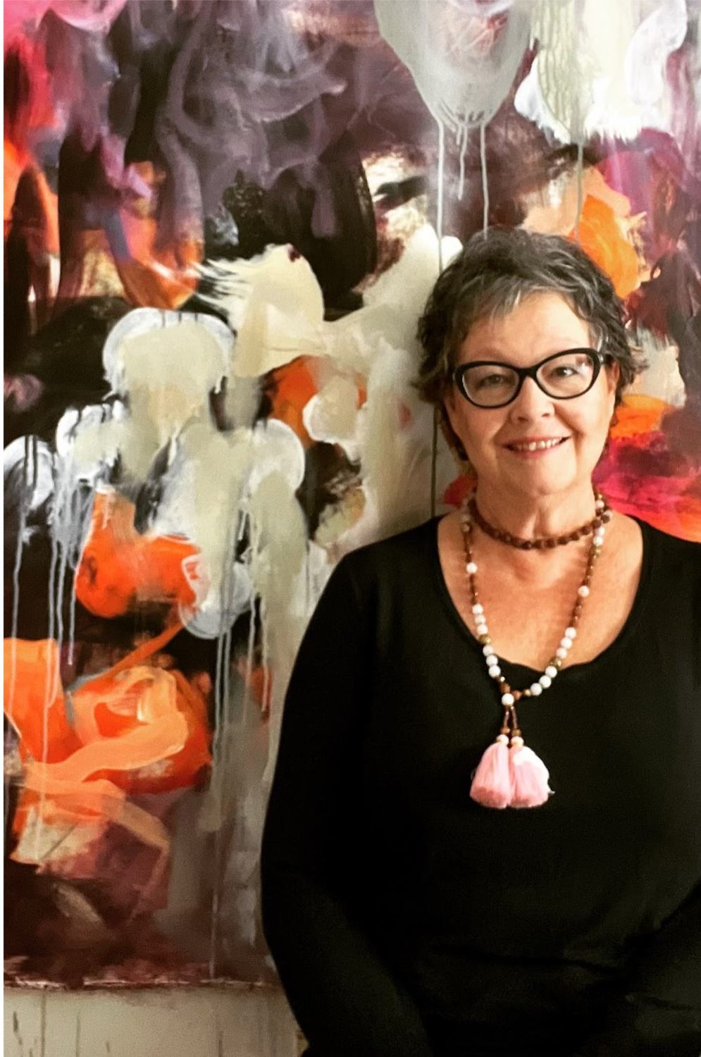 Artist Jackie DeBlasio stands beside large abstract painting with text about her exhibition.