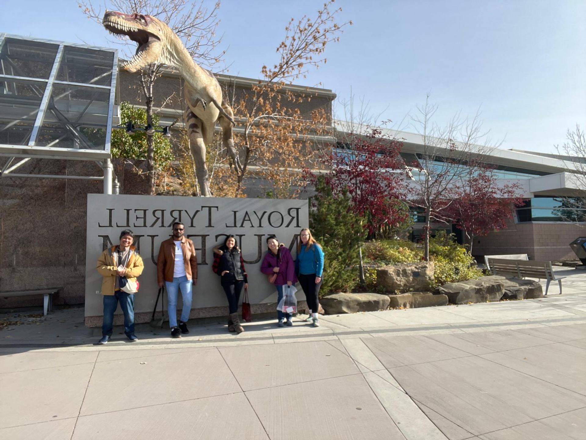 Visitors stand outside a museum beneath a towering dinosaur sculpture near the entrance.