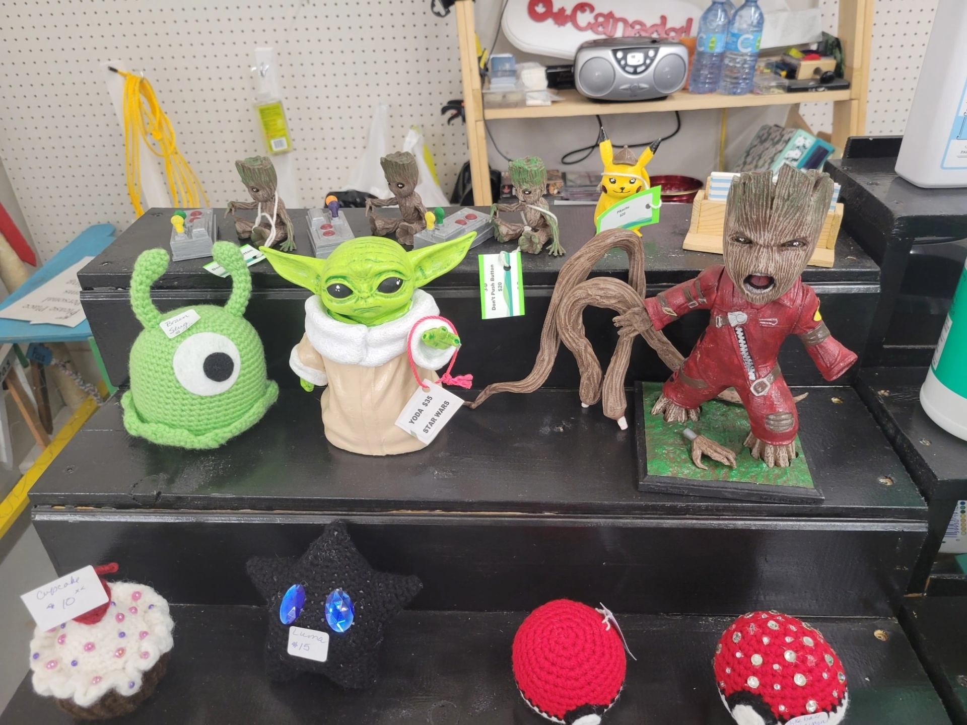 Display of handmade character figures and crocheted items arranged on tiered black shelves.