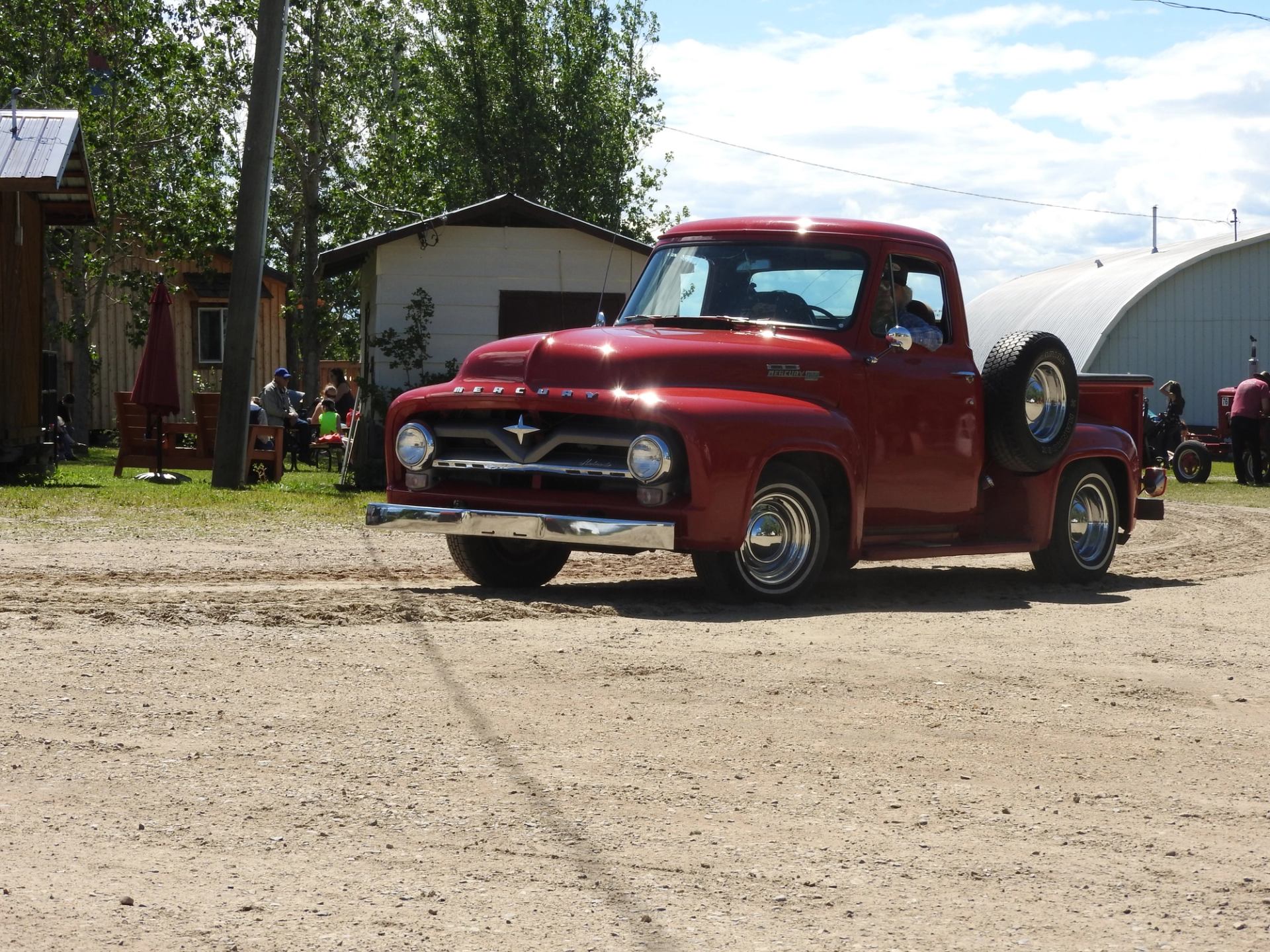 Red vintage pickup truck with chrome grille and star emblem in museum courtyard.