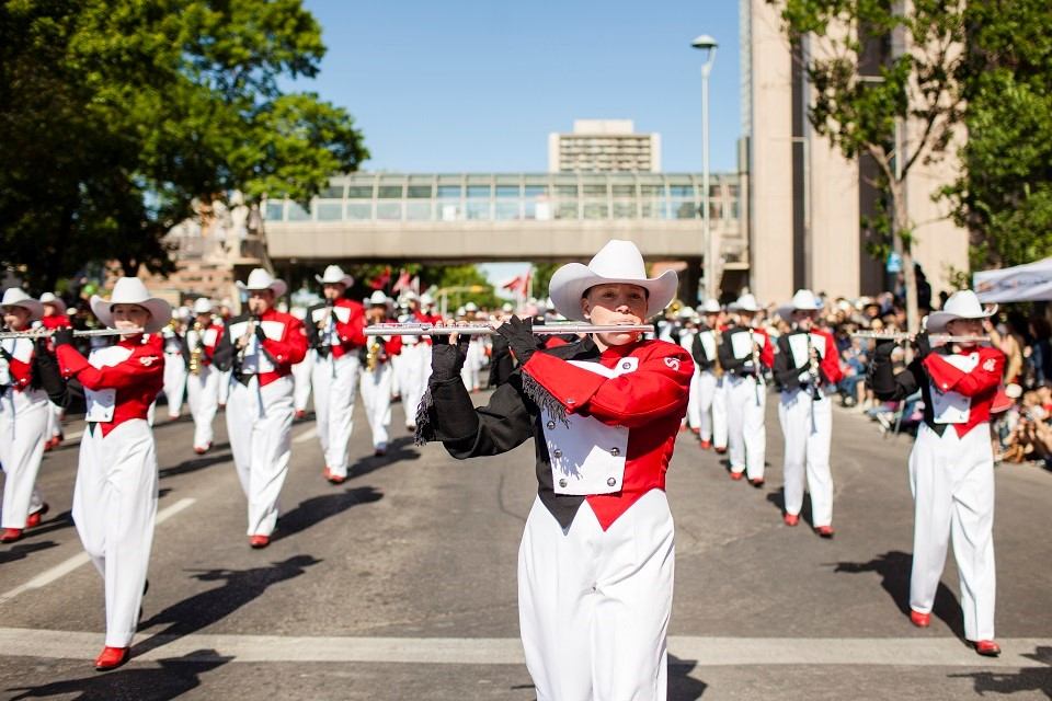 Marching band performs in Calgary Stampede Parade on city street.