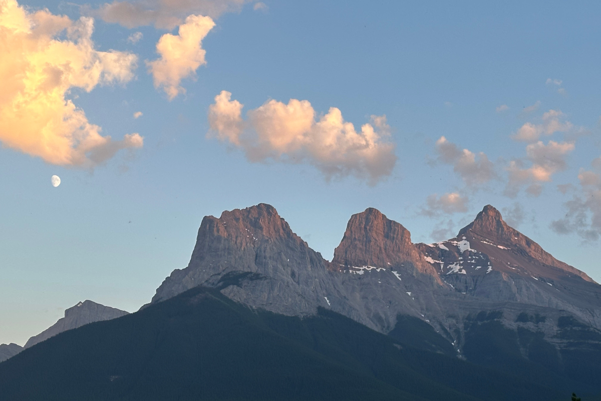 Mountain peaks with snow patches under a blue sky with scattered clouds in the Canadian Rockies.