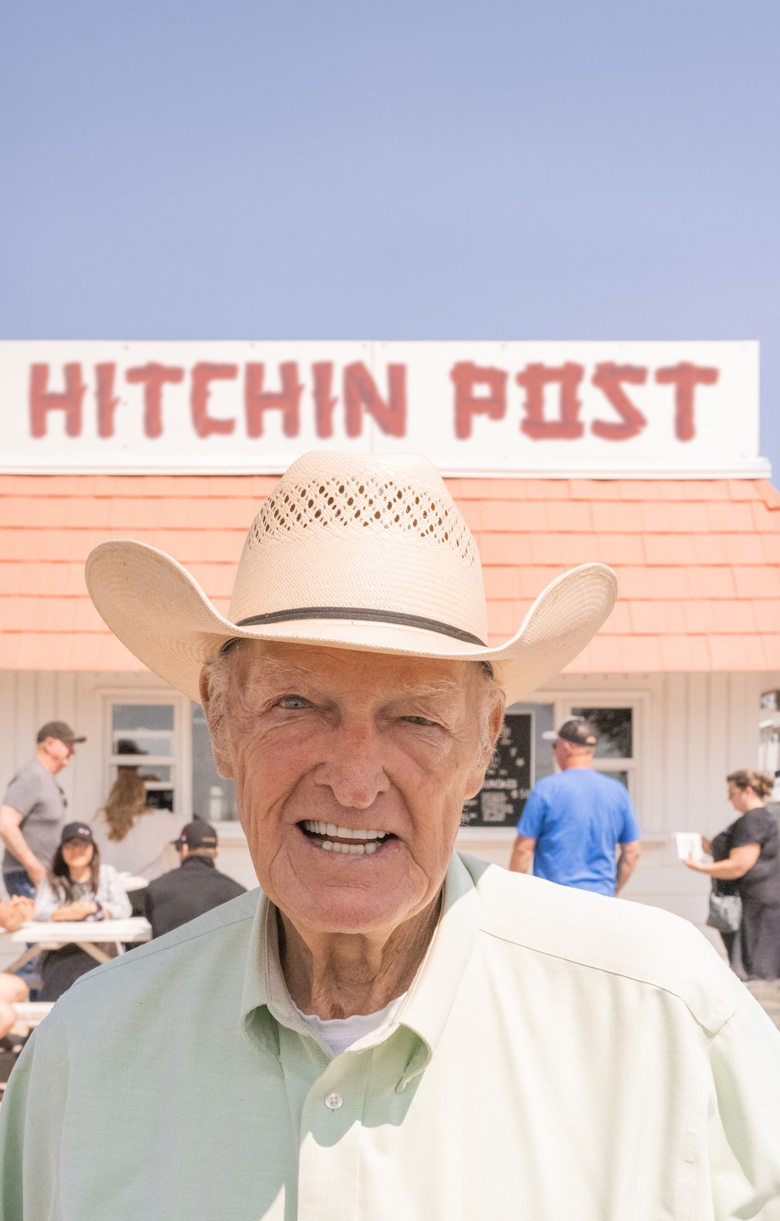 Cowboy hat and man in front of Hitchin Post sign at drive-in restaurant.